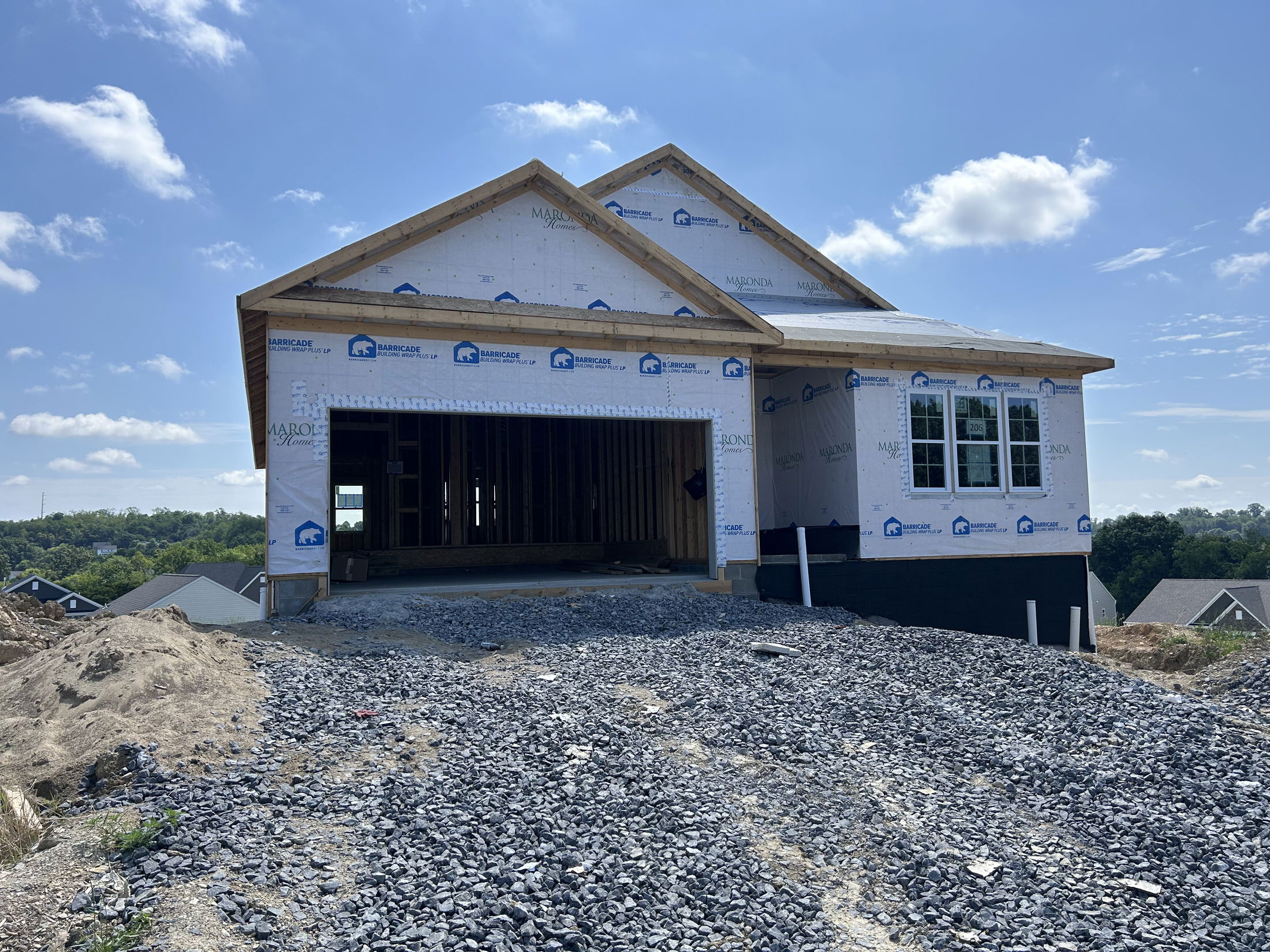 Newly constructed house with exposed framework and protective wrap, set on a hill under a clear blue sky.