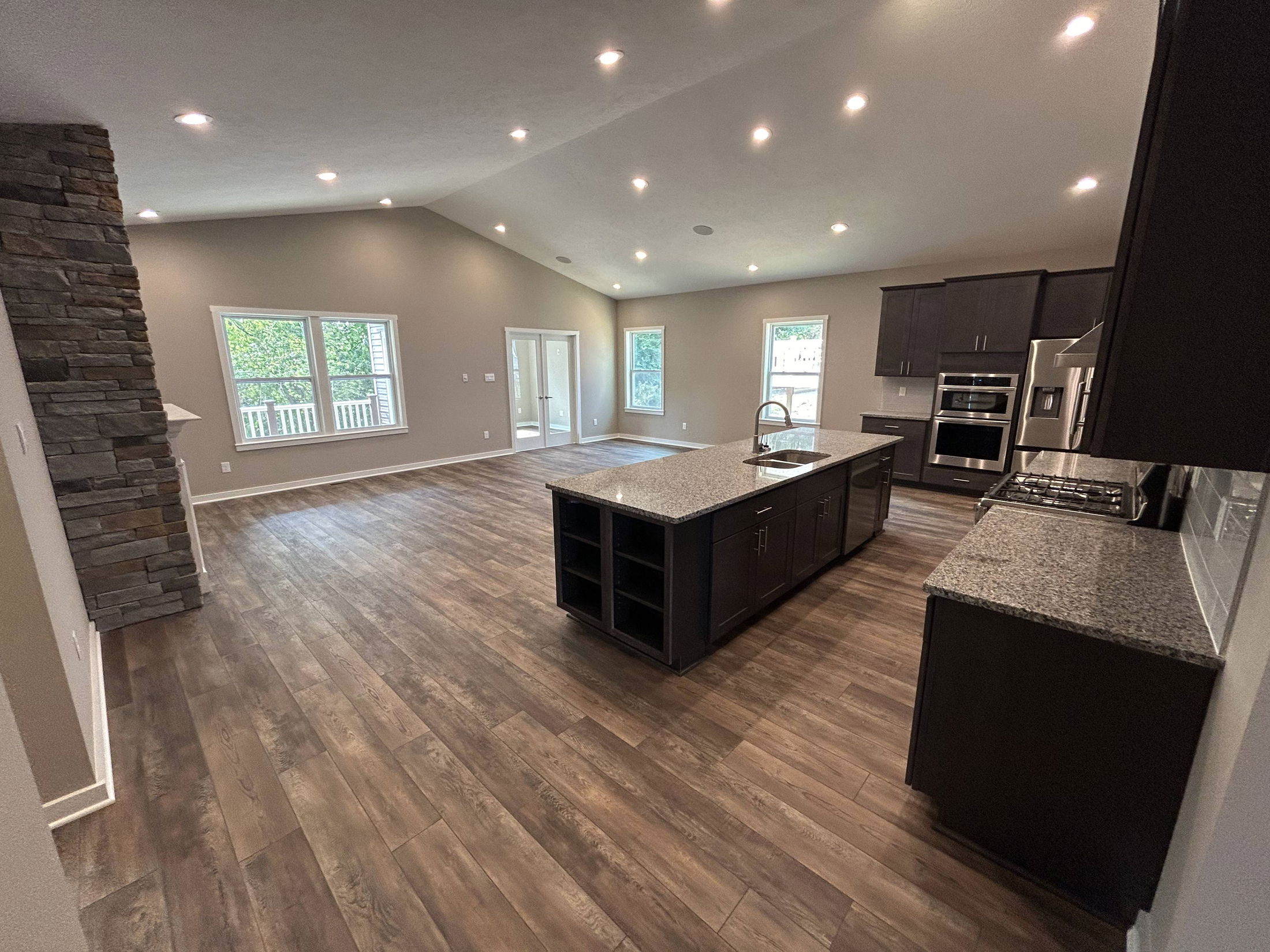 Modern open-concept kitchen and living room with hardwood floors, dark cabinets, granite countertops, and recessed lighting.
