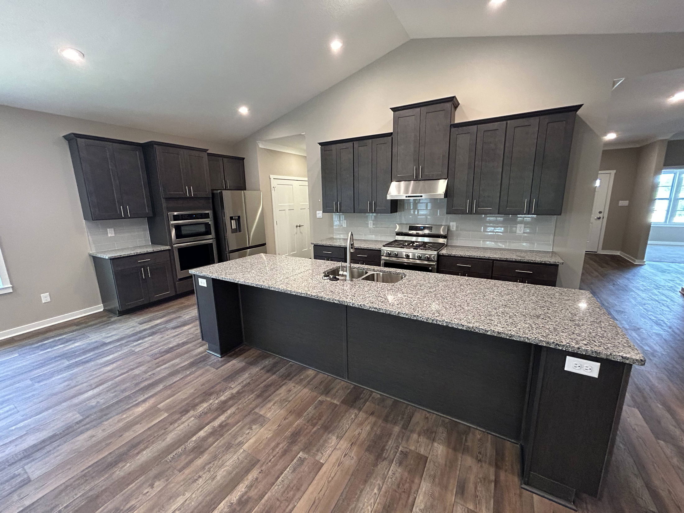 Modern kitchen interior with dark wood cabinets, granite countertops, stainless steel appliances, and hardwood floors.
