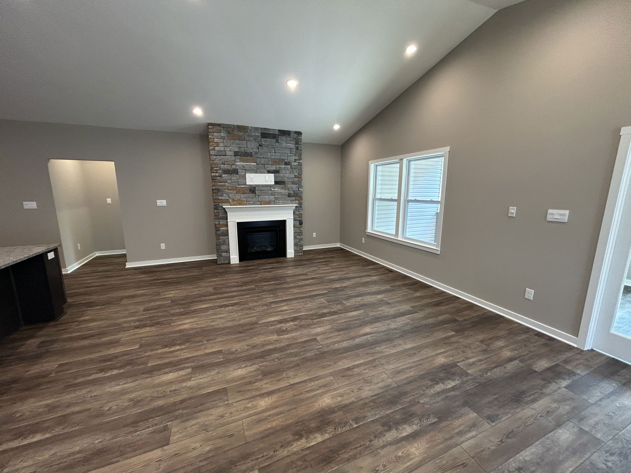 Spacious modern living room with vaulted ceiling, stone fireplace, large windows, and wood flooring.
