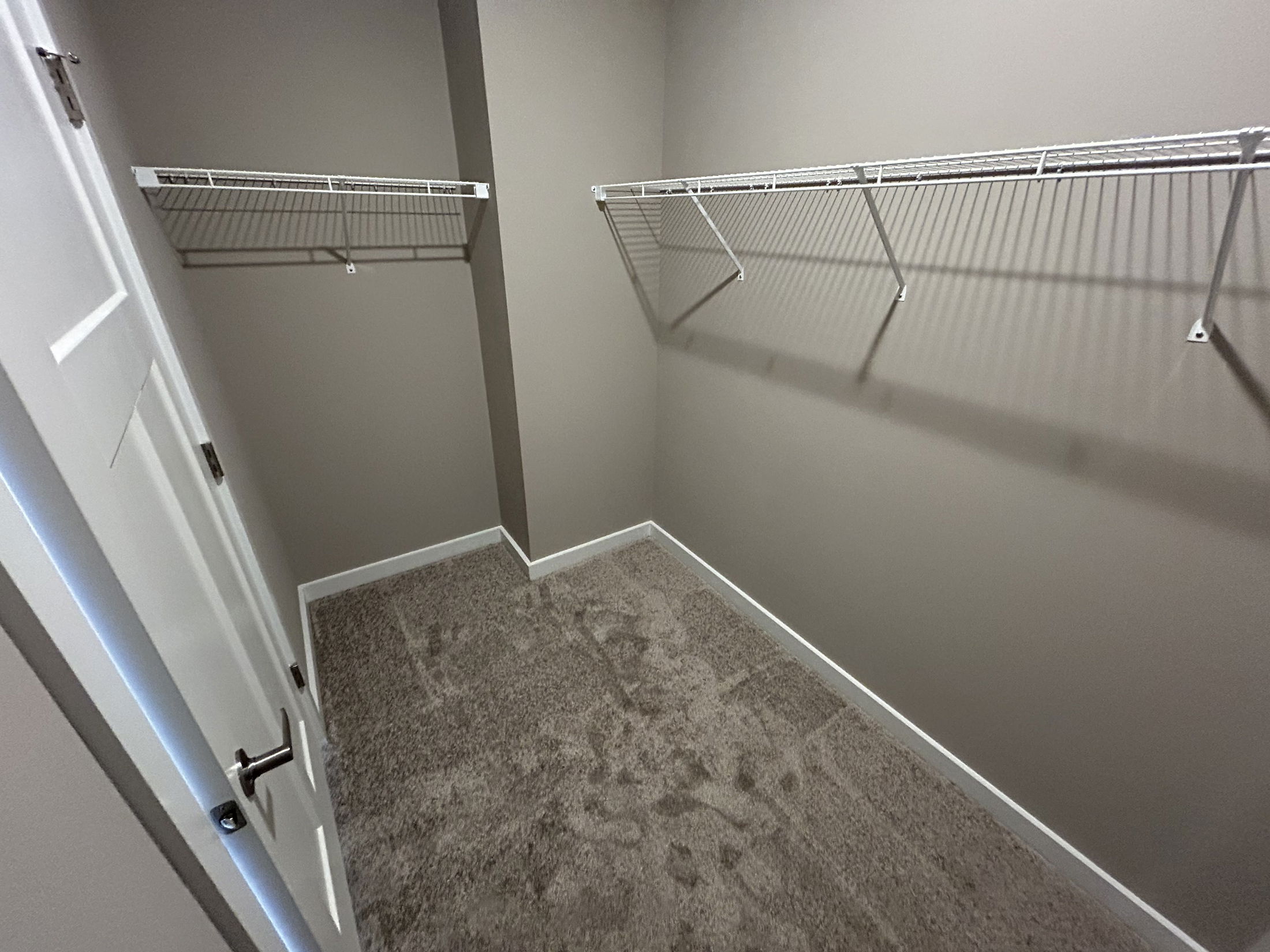 Empty walk-in closet with white wire shelving and beige walls.