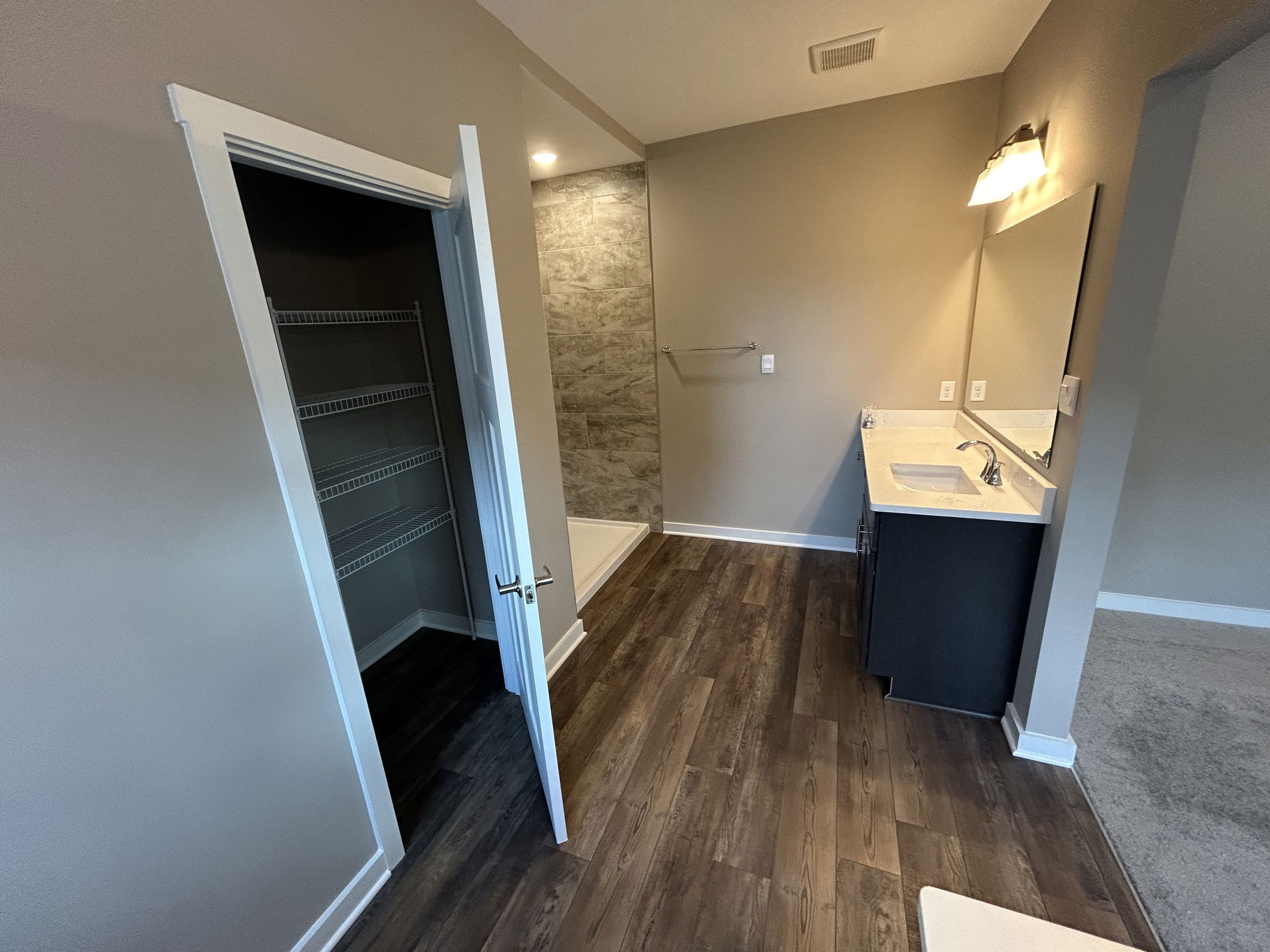 Modern bathroom with wood flooring, open closet, and sleek vanity under warm lighting.