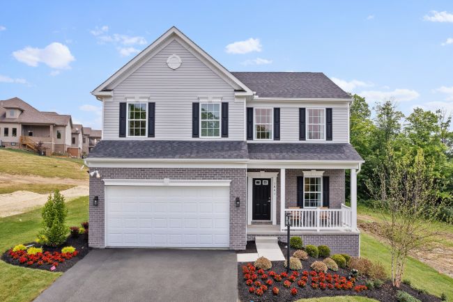 Front view of a modern two-story suburban house with a neatly landscaped yard, featuring a brick facade and attached garage.