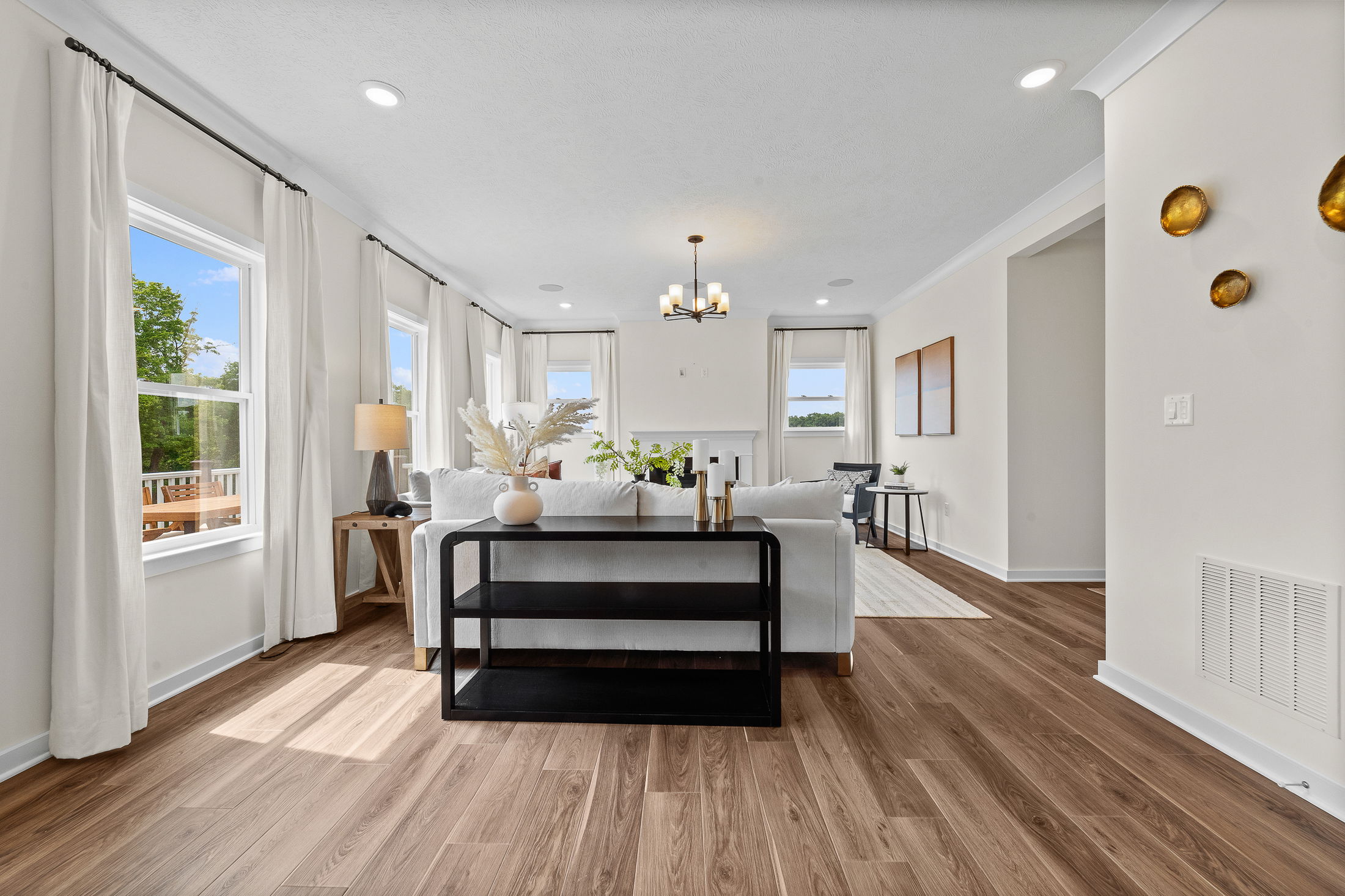 Bright and modern living room with wooden flooring, elegant white furniture, large windows, and stylish decor accents.