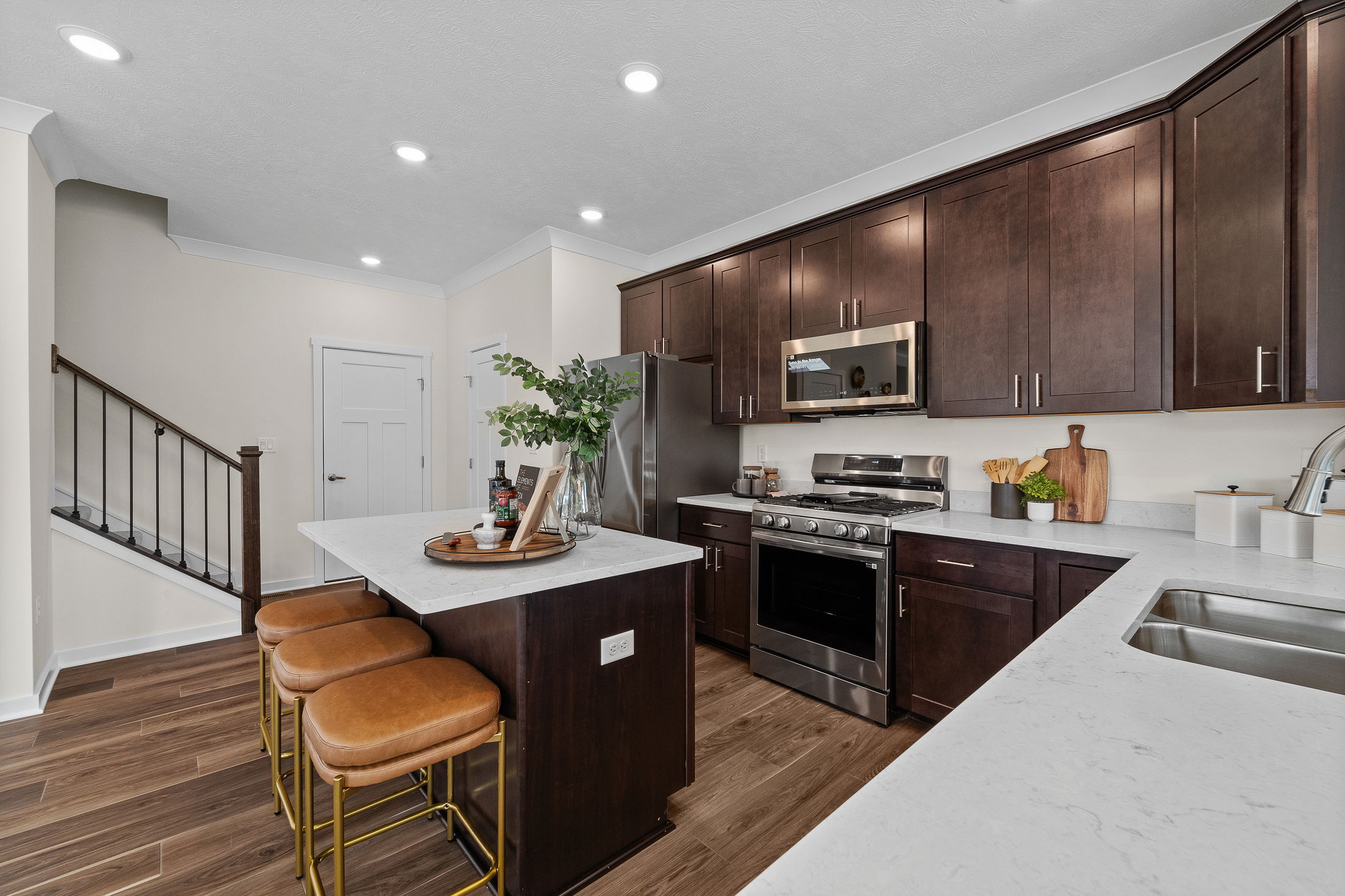 Modern kitchen with dark wood cabinets, stainless steel appliances, and a white marble island with leather barstools.