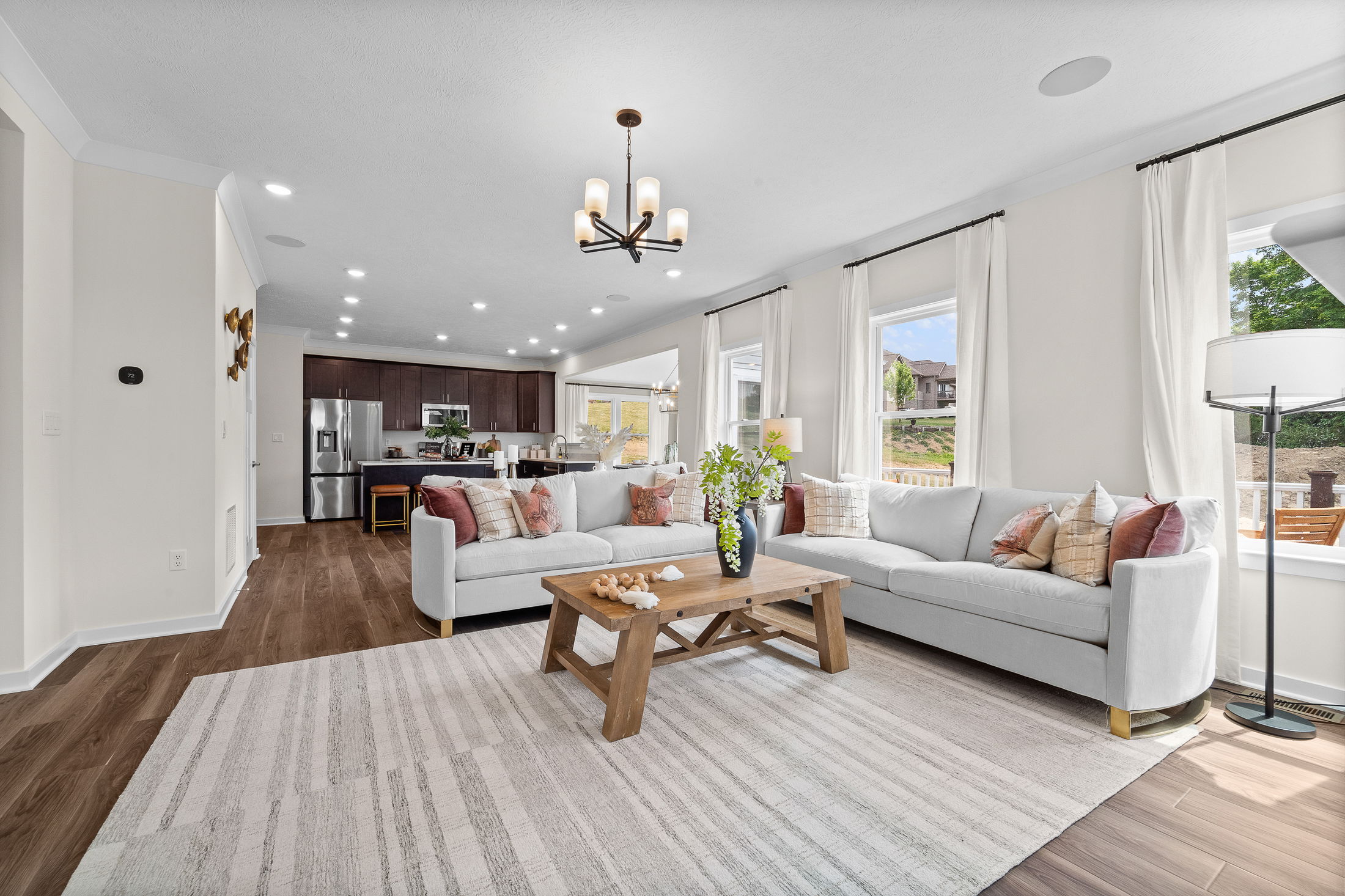 Modern open-concept living room with stylish white sofas, wooden coffee table, and integrated kitchen area.