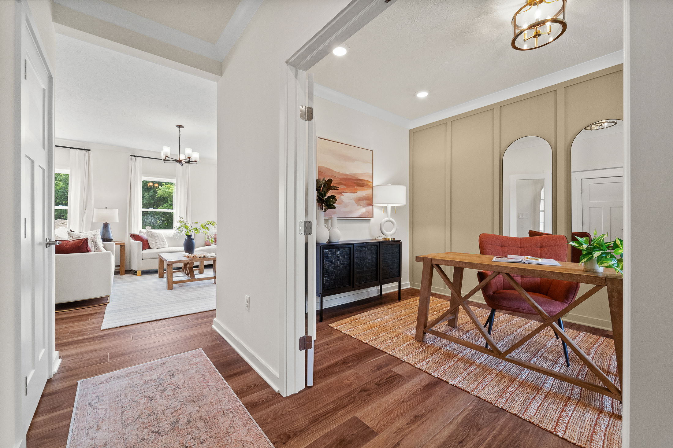 Modern home office with a wooden desk, red chair, and stylish living room in the background.