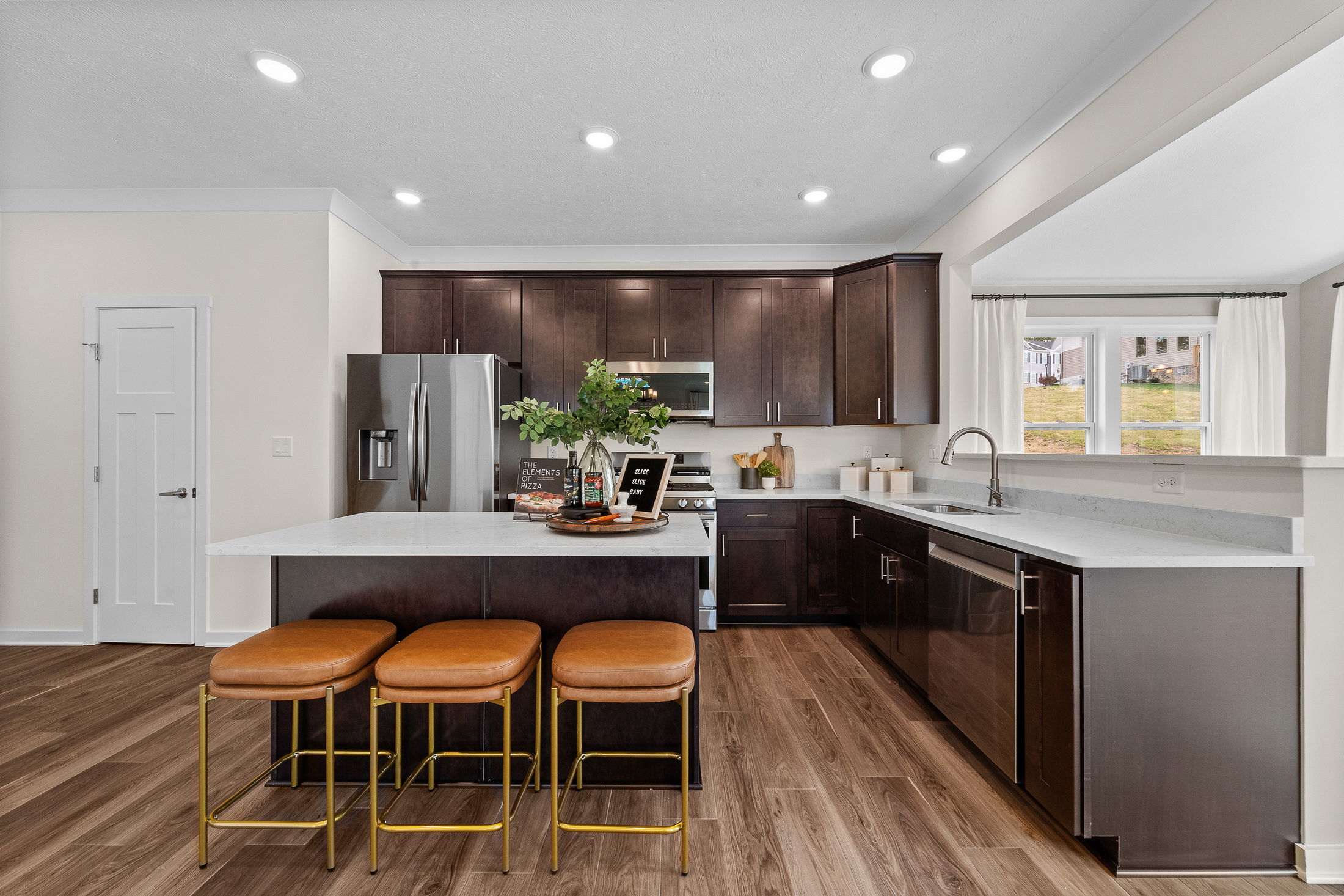 Modern kitchen with dark wood cabinets, stainless steel appliances, a central island with bar stools, and hardwood flooring.