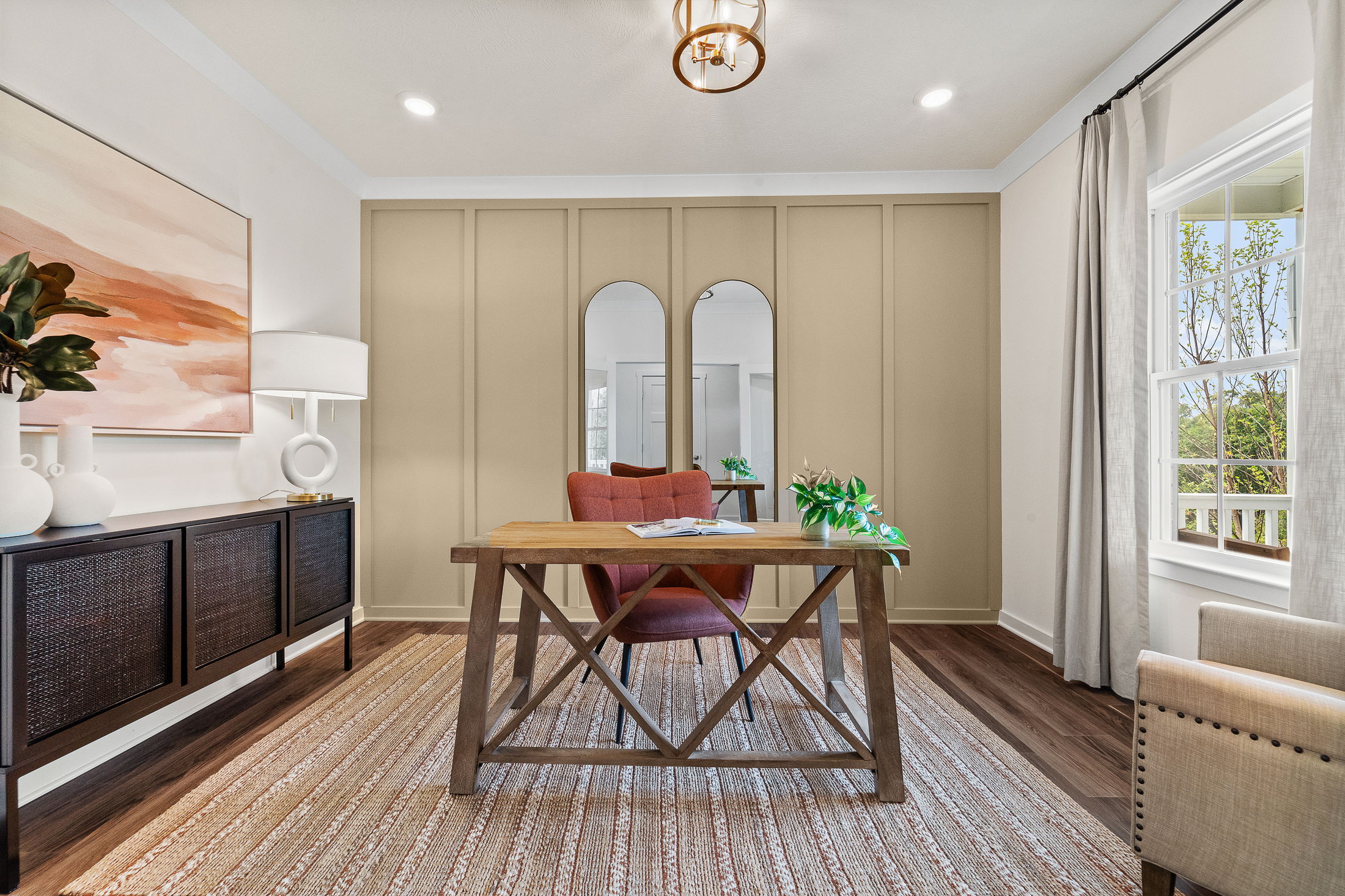 Elegant home office interior featuring a wooden desk, modern art, and large windows with natural light.