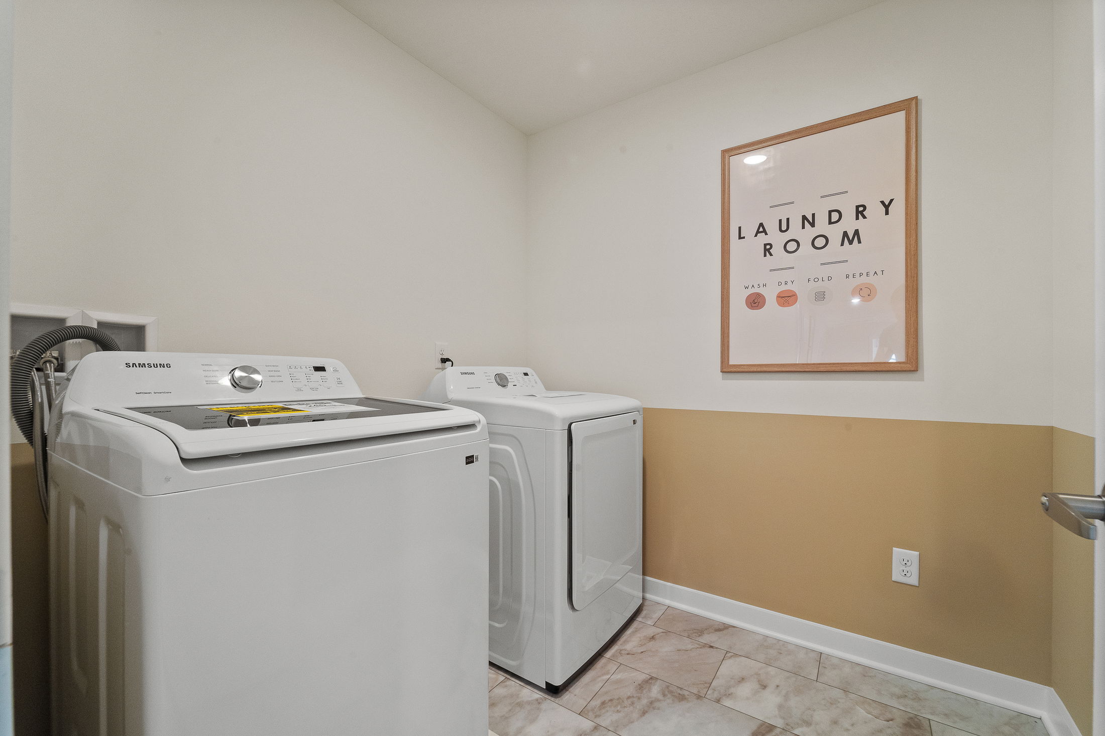 Modern laundry room with Samsung washer and dryer, featuring tiled floor and a decorative 