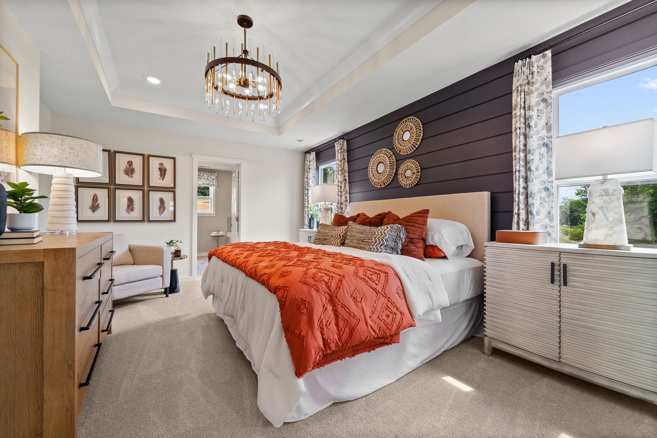Modern bedroom with cozy bed, stylish orange bedding, decorative wall art, and elegant chandelier lighting.