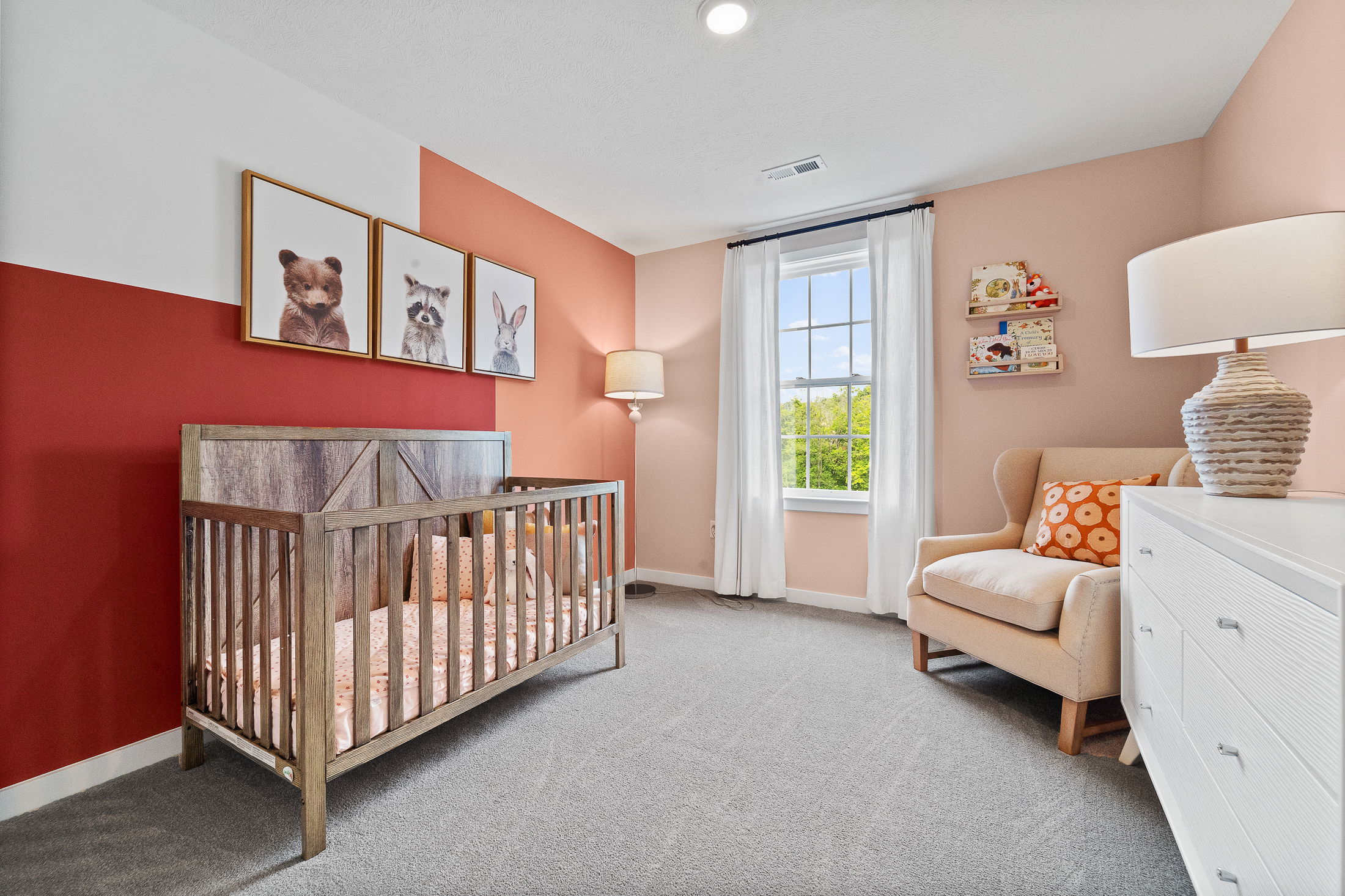 Cozy nursery room with a wooden crib, animal wall art, an armchair with an orange pillow, and a dresser under soft lighting.