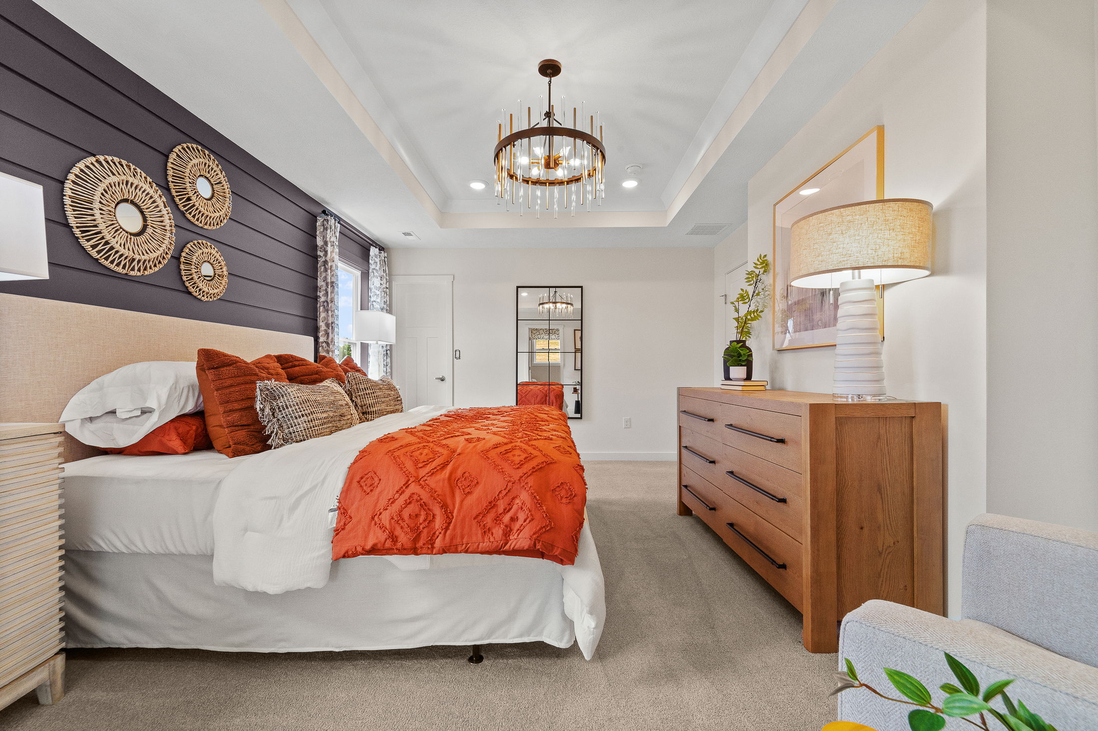 Modern bedroom with a stylish chandelier, orange bedding, wood accents, and decorative wall art.