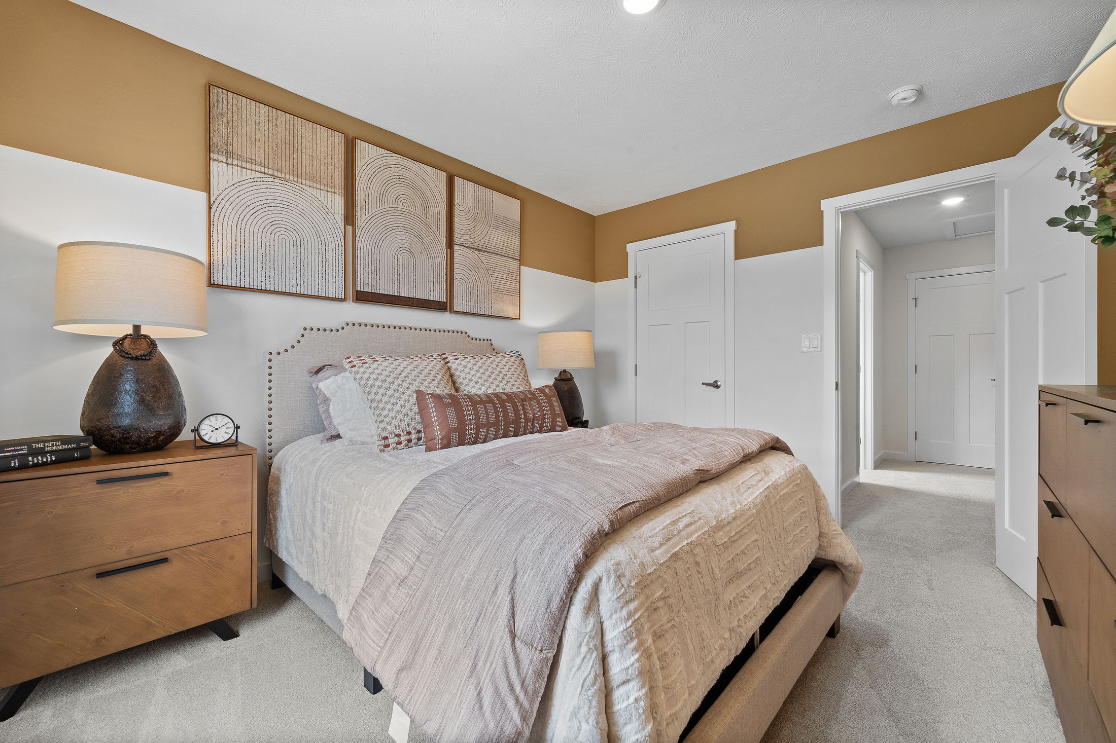 Modern bedroom with beige and white decor, featuring a stylish bed, wooden nightstands, and abstract wall art above the headboard.