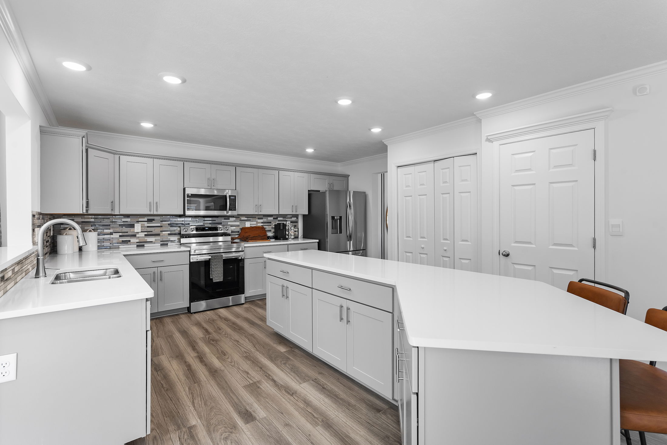 Modern kitchen with white cabinets, stainless steel appliances, and wood flooring.