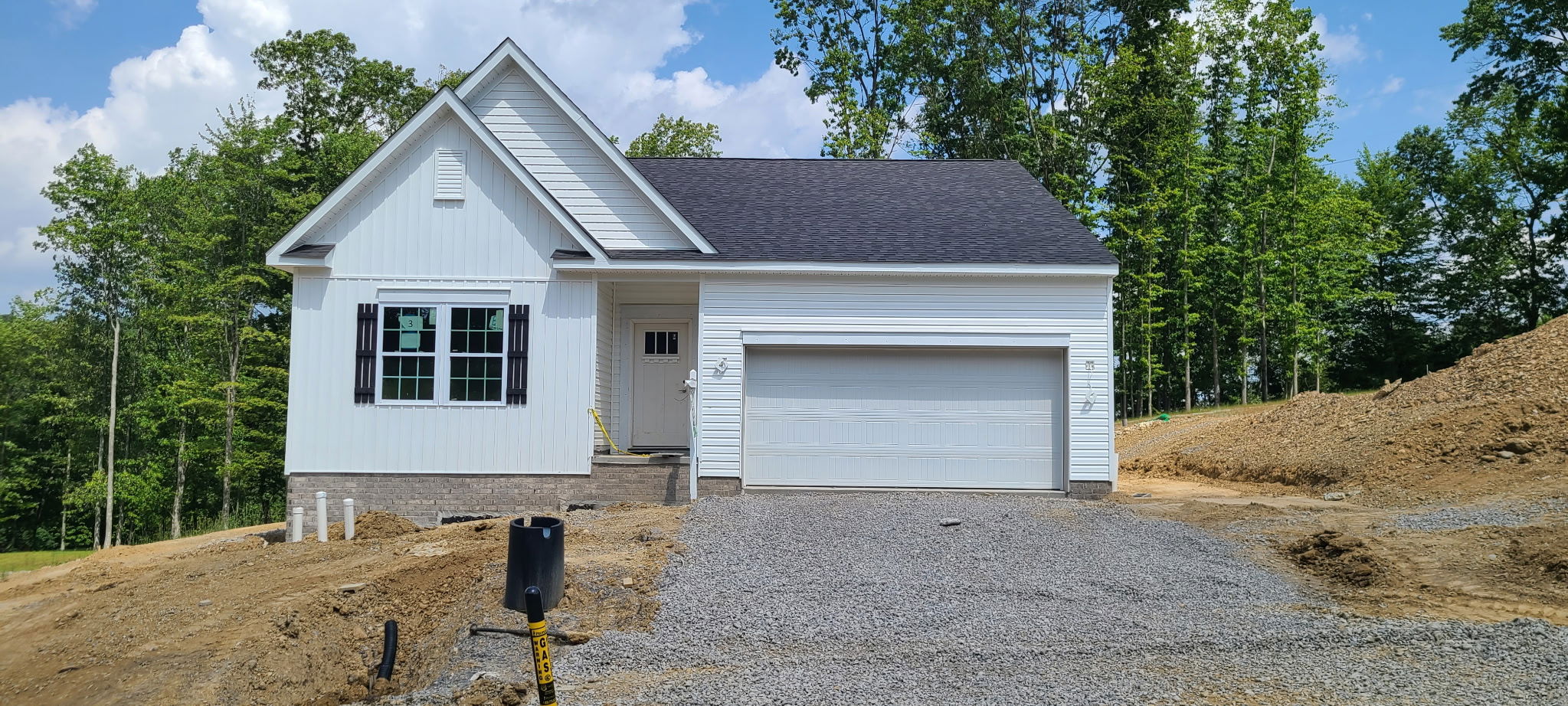 A newly constructed single-story white house with a two-car garage and gravel driveway, surrounded by trees and a clear blue sky.