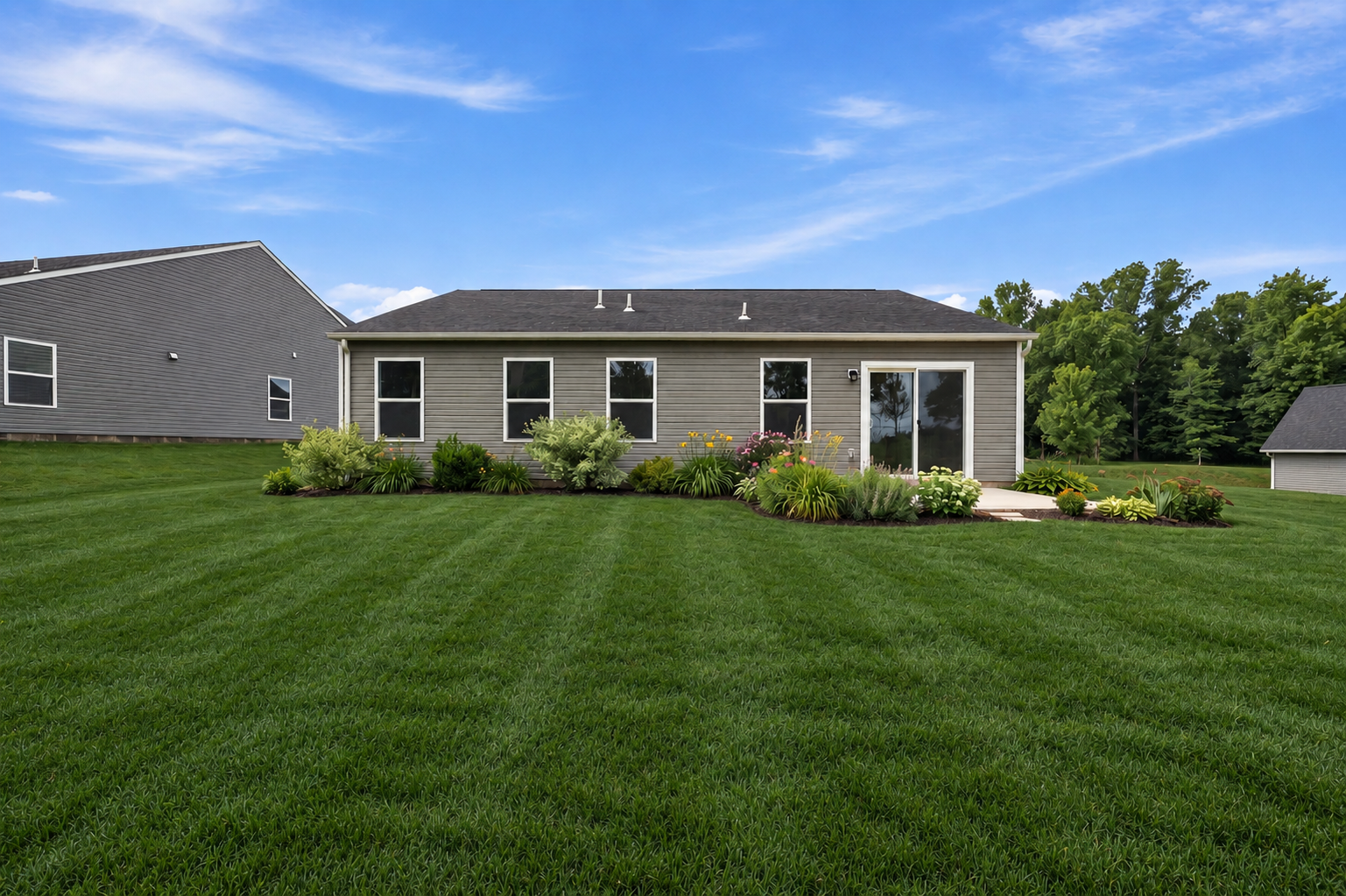 A well-maintained backyard featuring a lawn, flower beds, and a house with a sliding glass door.