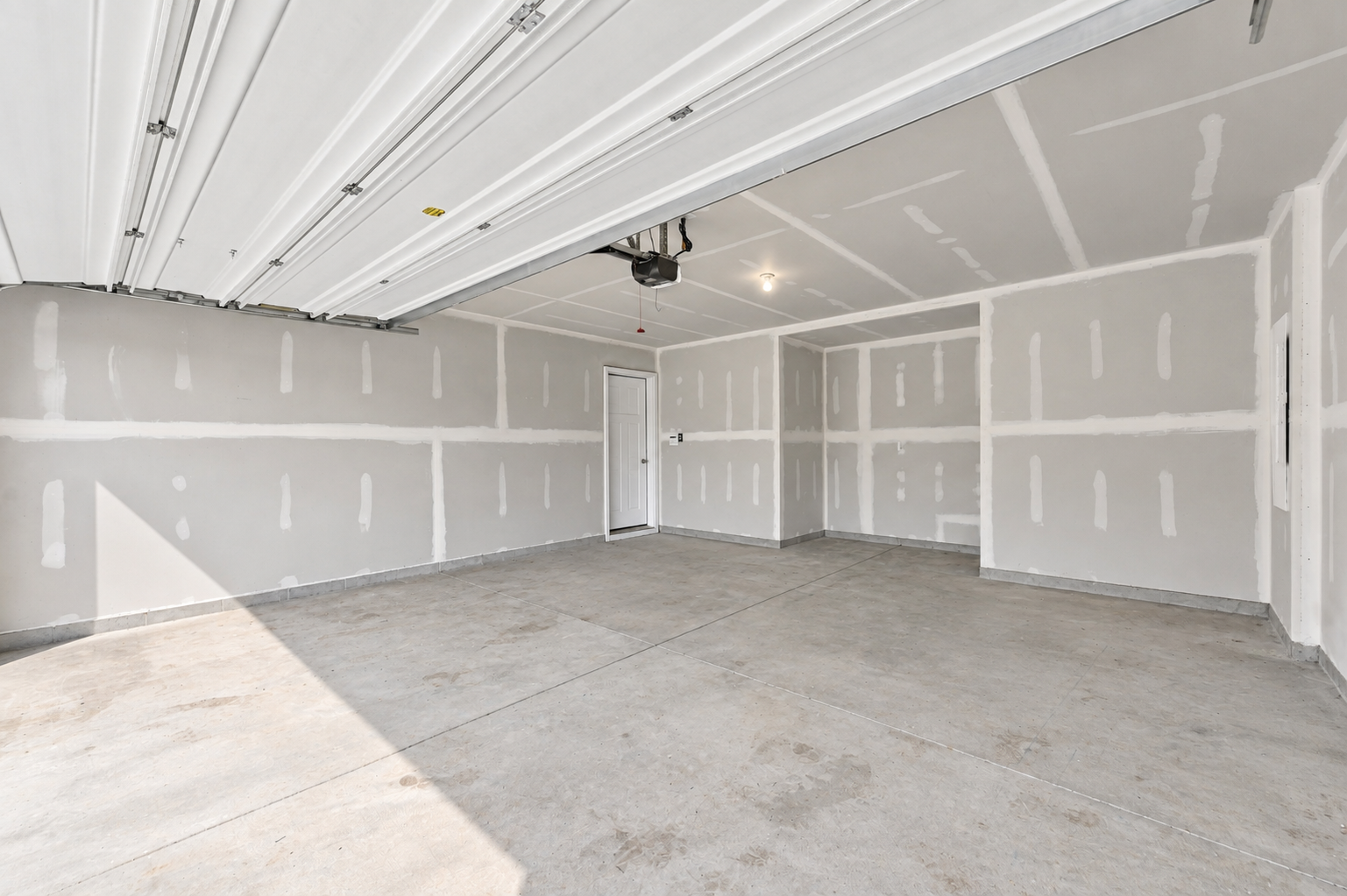 A spacious empty garage with unfinished drywall and a concrete floor.