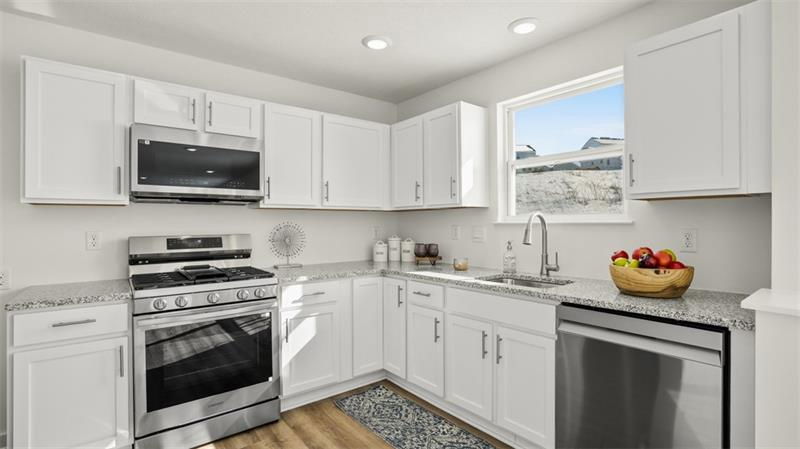 Modern kitchen with white cabinets, stainless steel appliances, and granite countertops featuring a bowl of fruit on the counter.