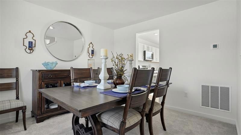 A stylish dining room featuring a wooden table set for four, accentuated by a round mirror and soft furnishings in a light, airy setting.