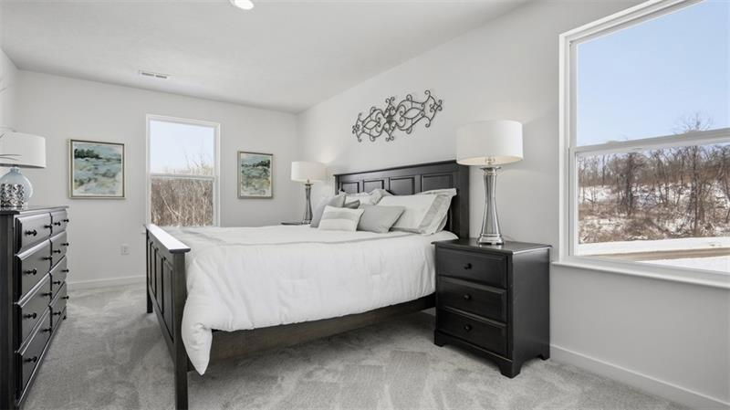 Modern bedroom featuring a black wooden bed, light gray bedding, and stylish decor with large windows letting in natural light.