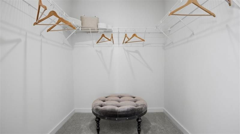 Modern walk-in closet featuring a plush ottoman, wooden hangers, and minimalist white shelving.