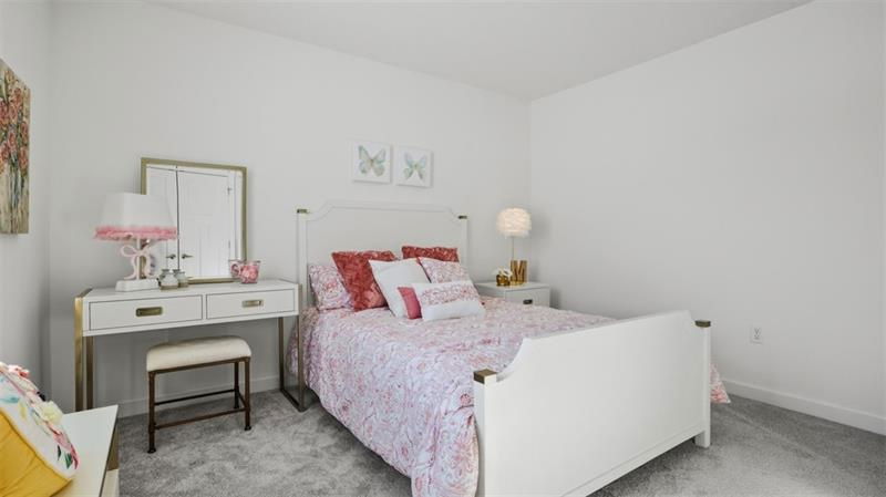 Bright and cozy bedroom featuring a white bed with floral bedding, a stylish desk, and decorative accents in soft colors.