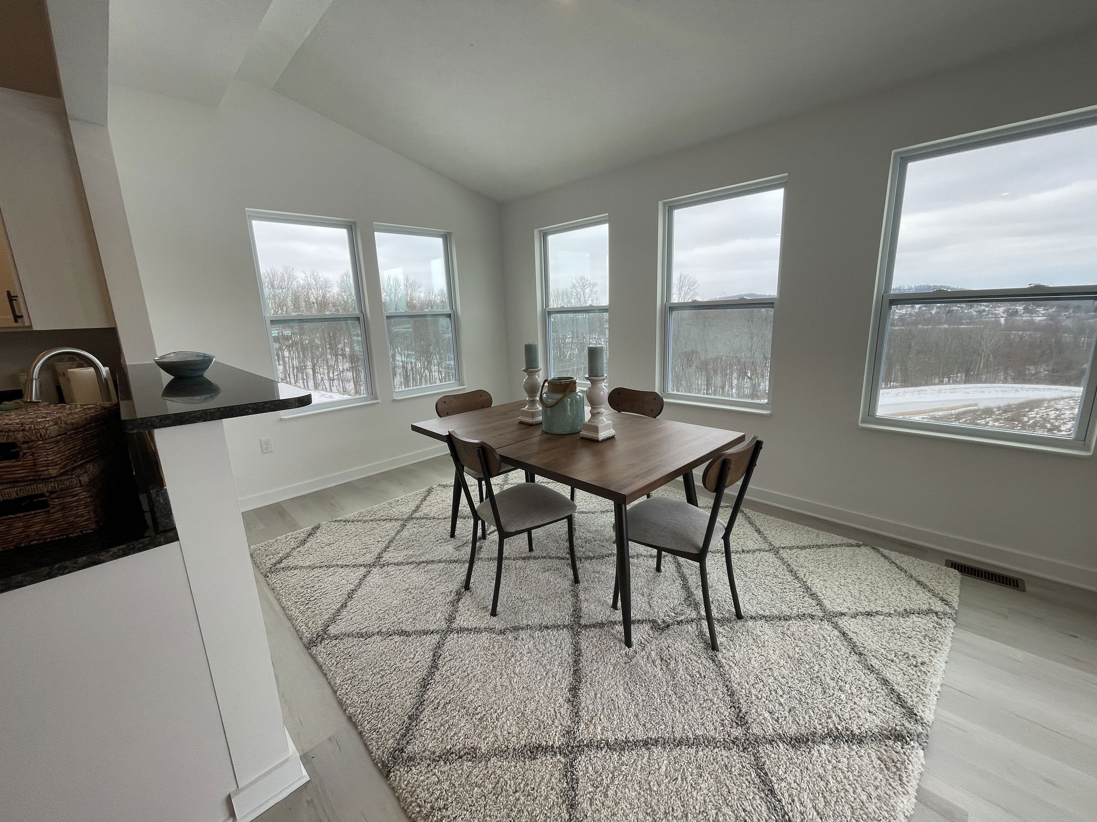 Modern dining room with large windows offering scenic views, featuring a wooden table and black chairs on a soft rug.