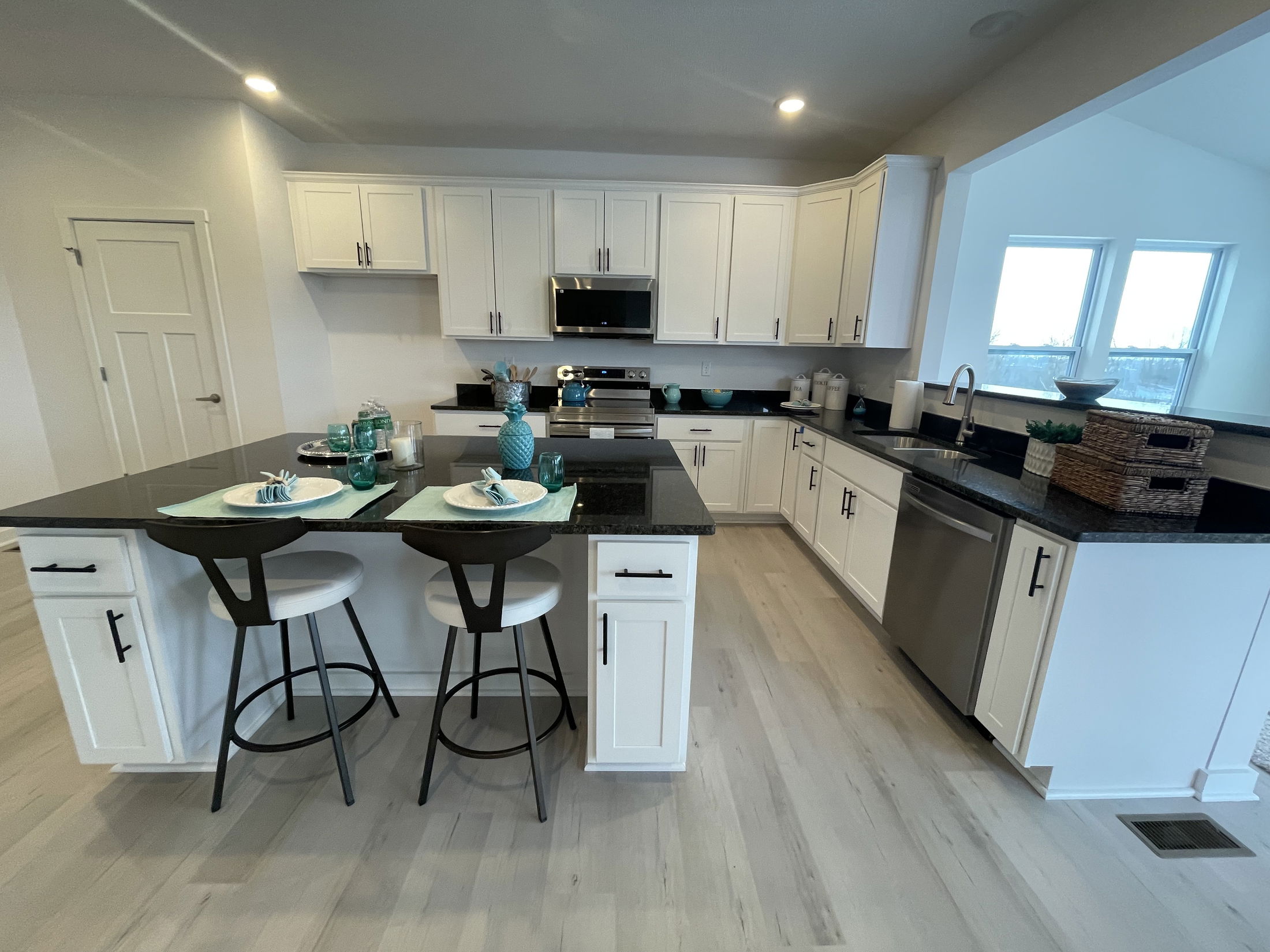 Modern kitchen featuring a dark granite countertop, white cabinetry, and stylish bar stools with decorative table settings.