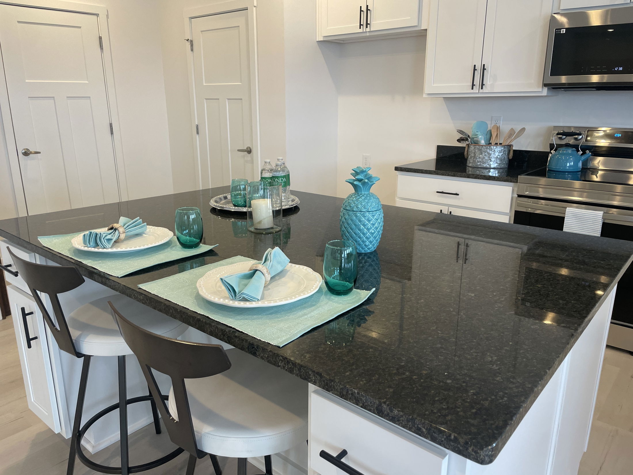 Modern kitchen with a black granite island, turquoise decor, and elegantly set dining table featuring plates and glasses.