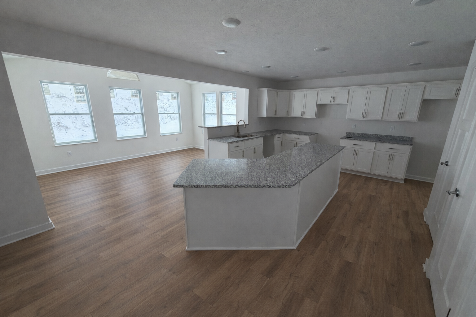 Spacious modern kitchen featuring a large granite island, white cabinetry, and abundant natural light from multiple windows.