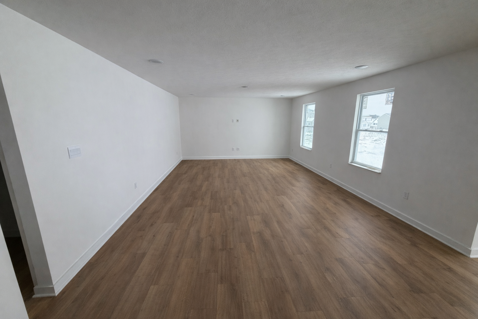 Spacious, empty living room with hardwood flooring and large windows providing natural light.