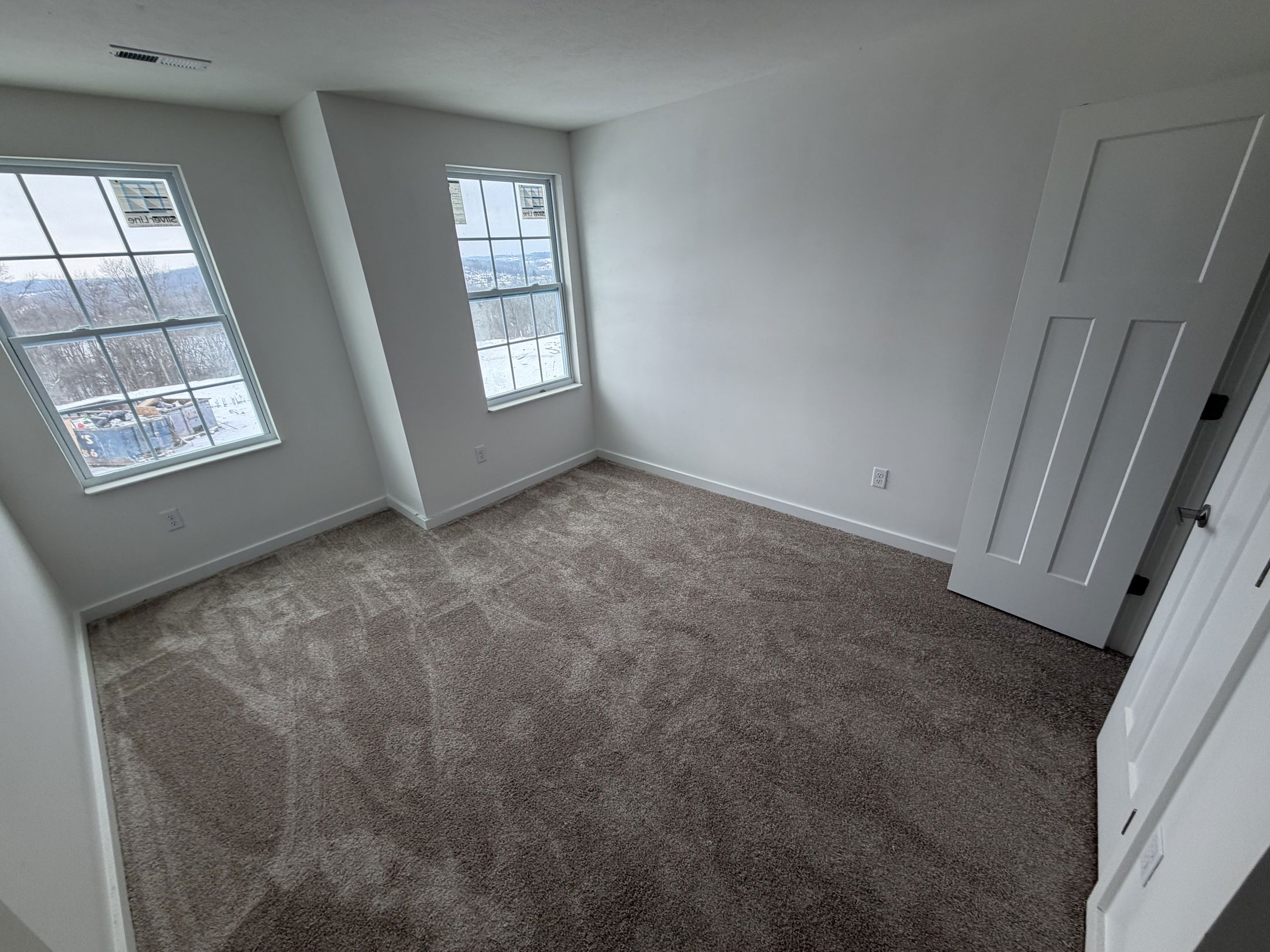 Empty modern bedroom with two large windows, freshly installed carpet, and white walls.