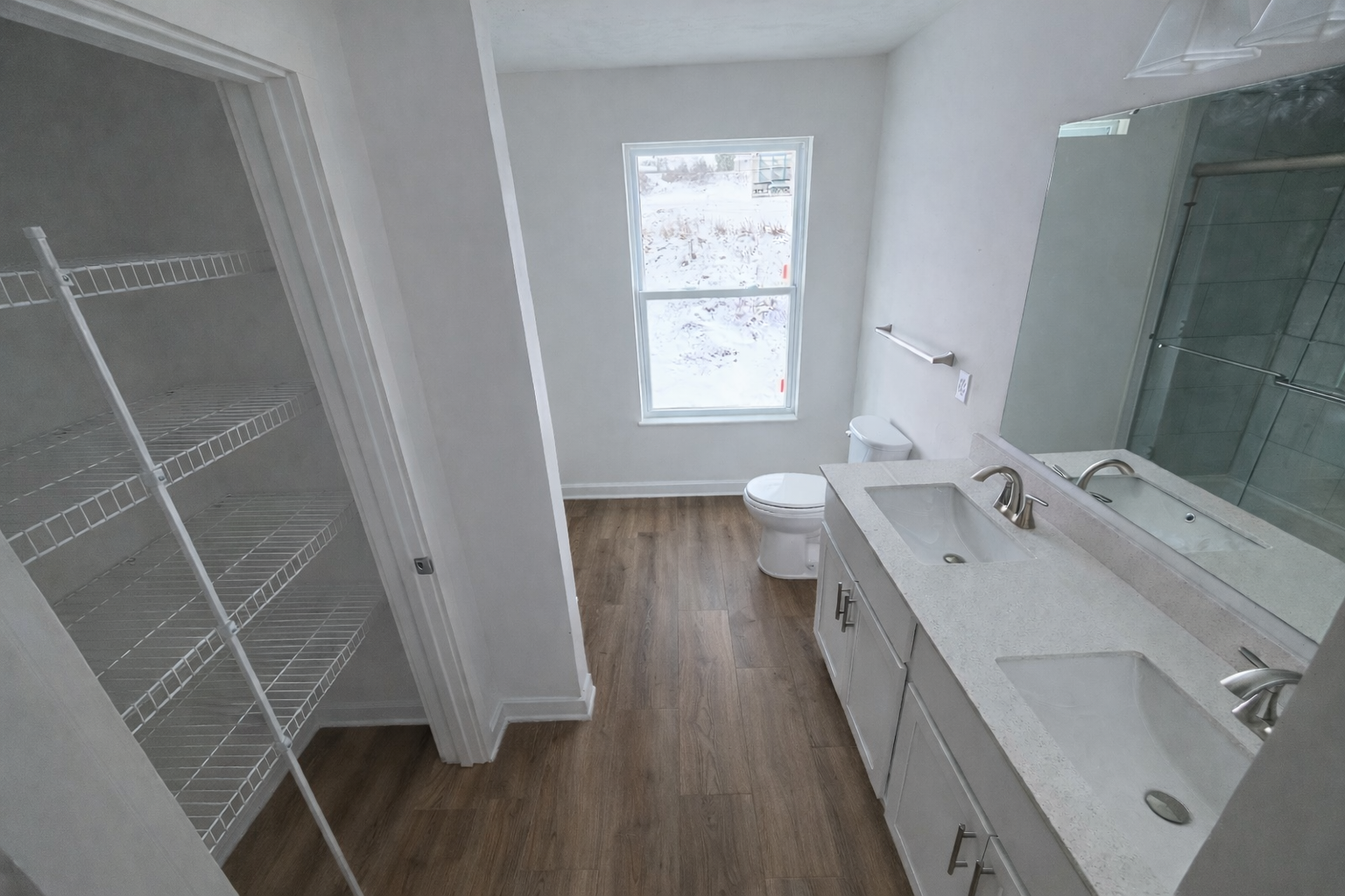 Bright and modern bathroom featuring double sinks, a window with snowy views, and a spacious closet with wire shelving.