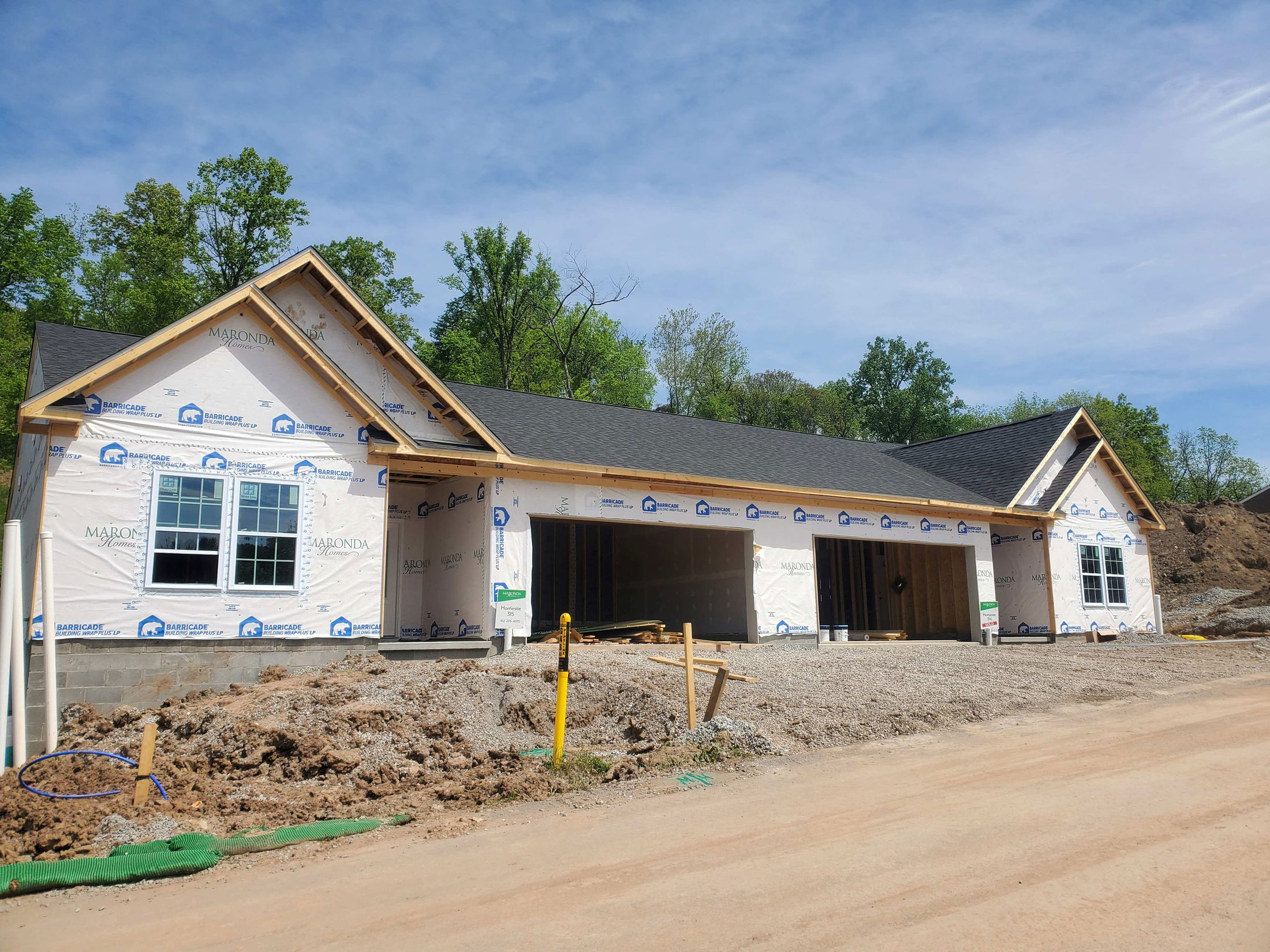 A new residential house under construction with visible framework and Maronda Homes branding, set against a clear blue sky and surrounded by trees.