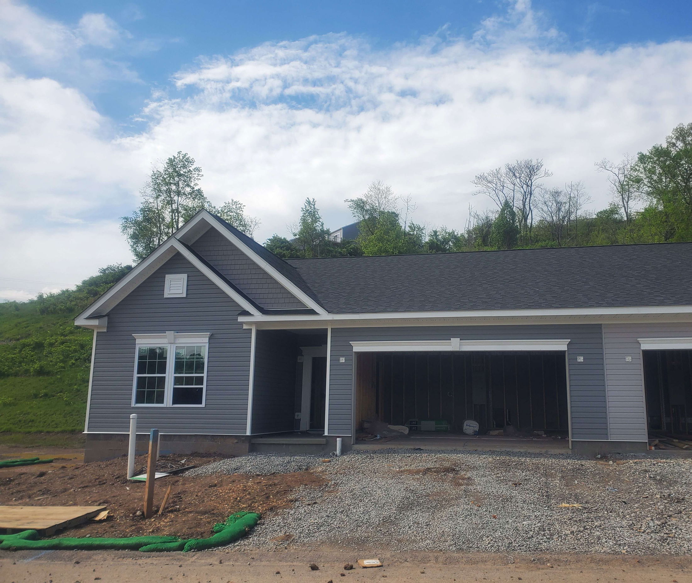 Newly constructed gray house with a double garage and unfinished front yard against a cloudy sky.