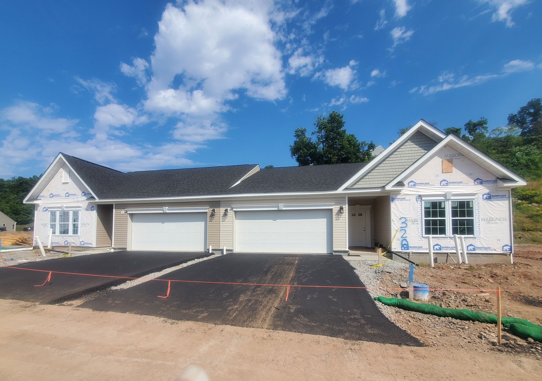 Newly constructed duplex with white garage doors and a shingle roof under a clear blue sky.