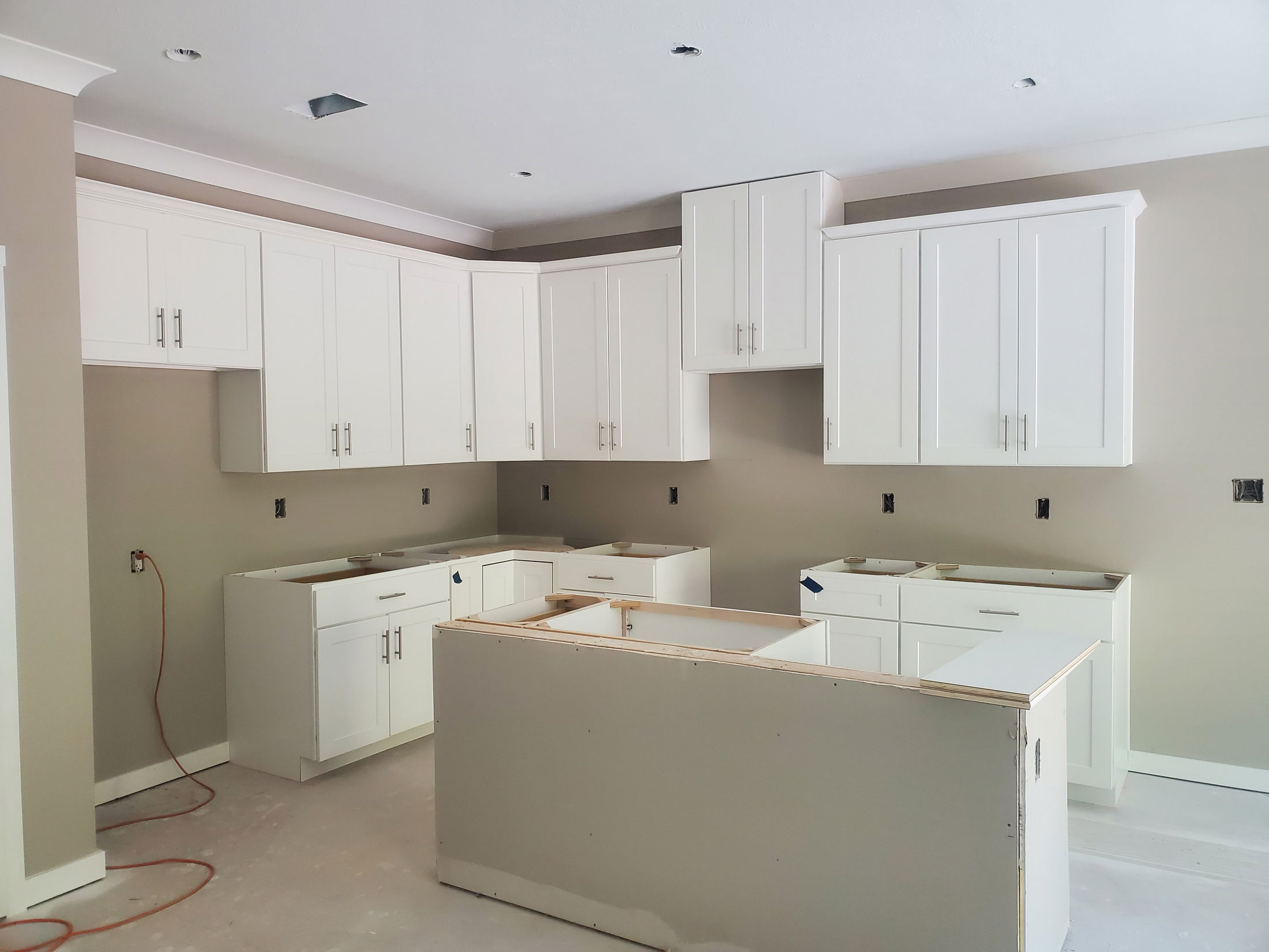 Modern kitchen under construction with white shaker cabinets and center island installation.