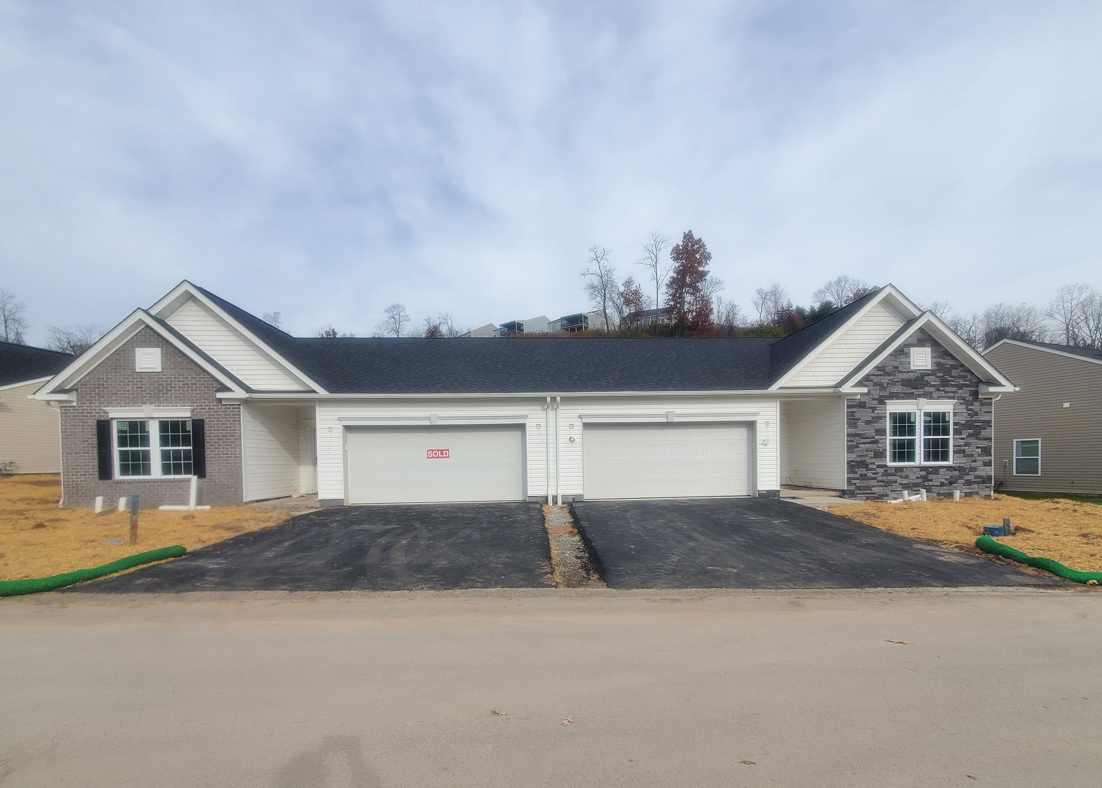 Newly sold duplex home with two garages and brick accents against a clear sky.