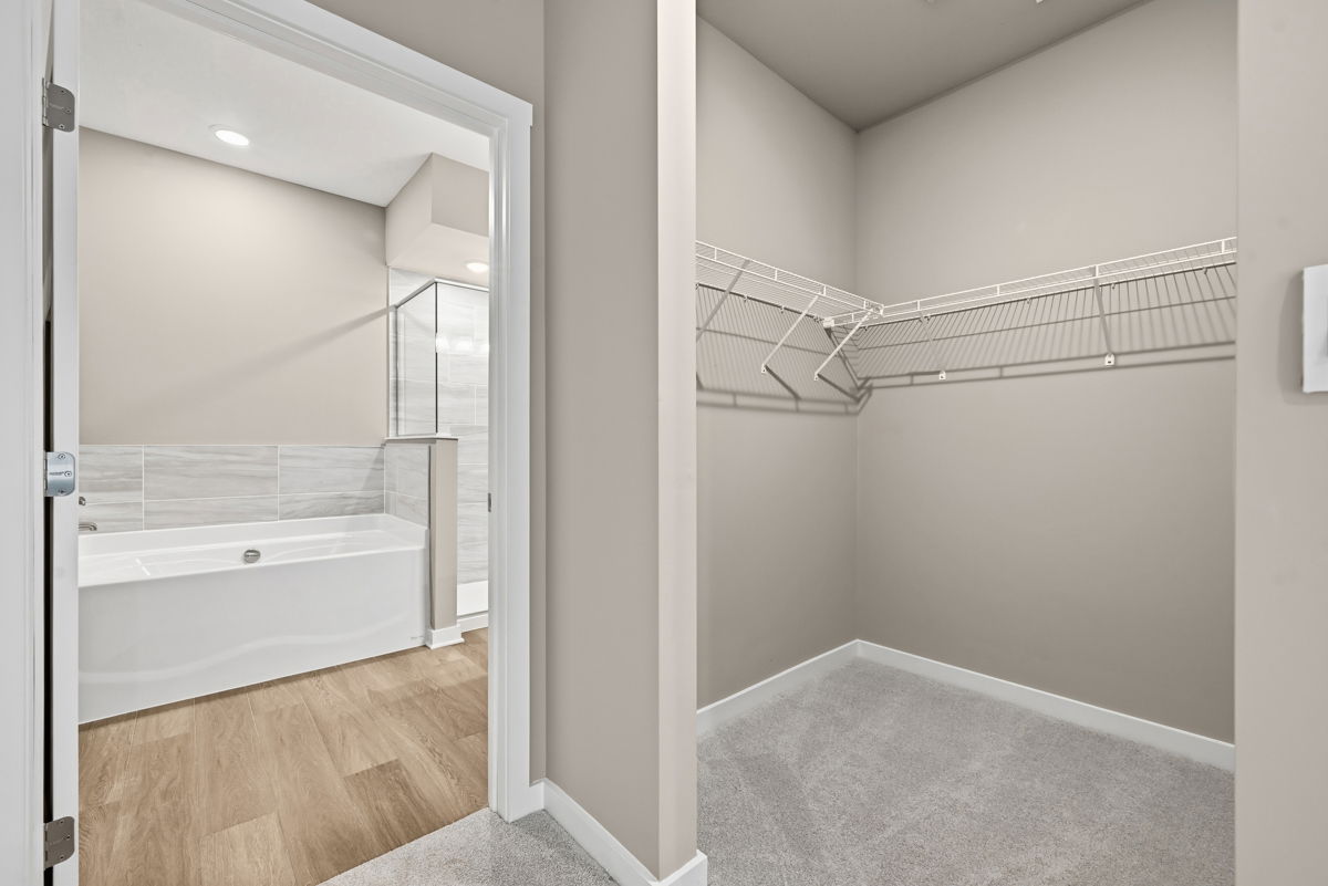Spacious bathroom with a white bathtub and an adjacent walk-in closet featuring wire shelving.