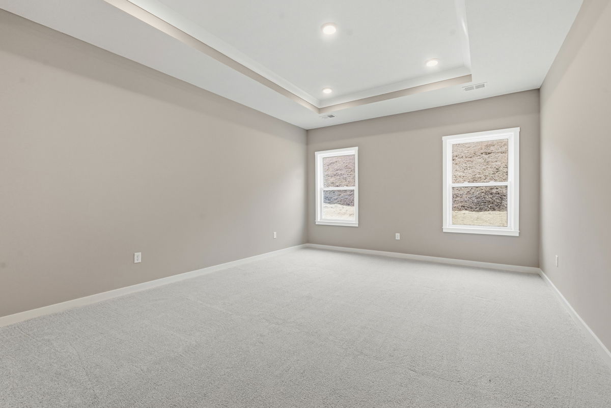 Spacious and bright empty bedroom with large windows and neutral wall colors showcasing carpet flooring.