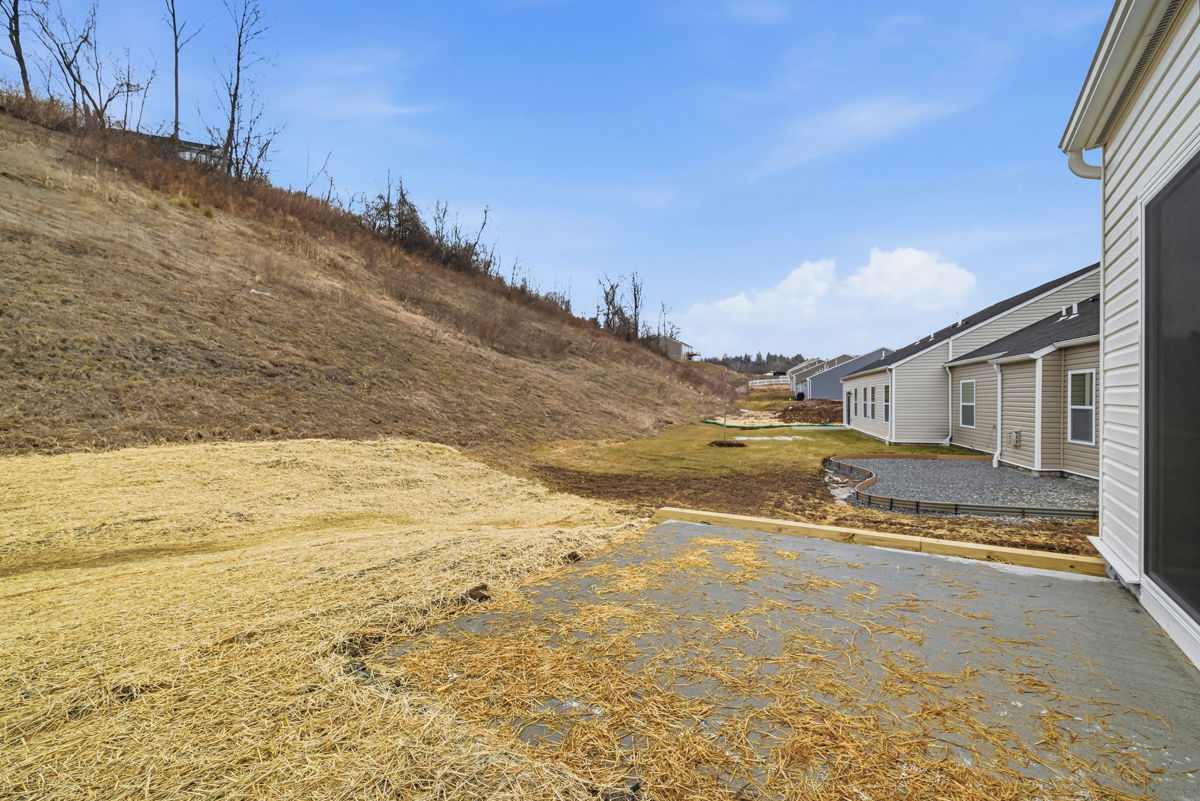 A scenic view of a sloped backyard featuring straw-covered ground and newly constructed homes under a clear blue sky.