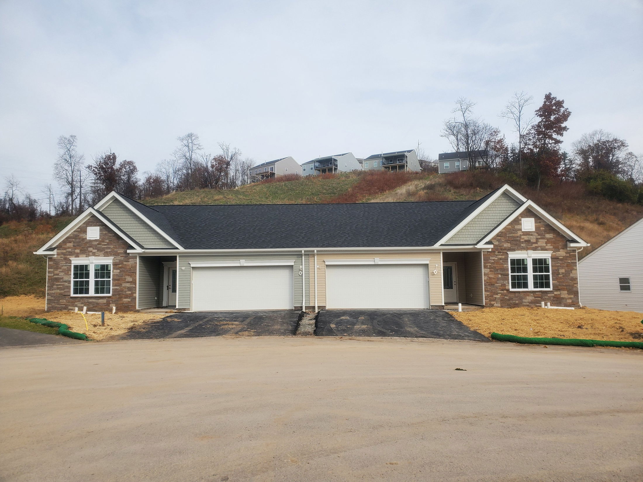 Newly constructed duplex with stone and siding exterior, featuring two double garages against a hillside.