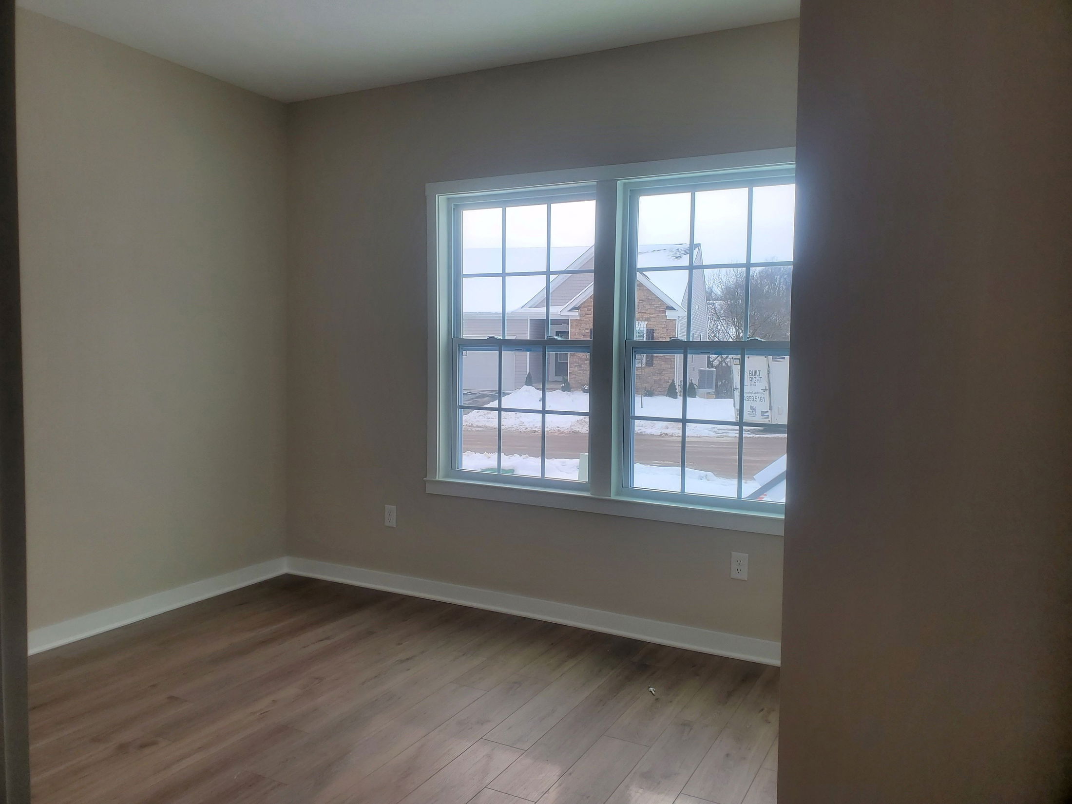 A bright, empty room featuring light brown walls and large windows overlooking a snowy landscape.