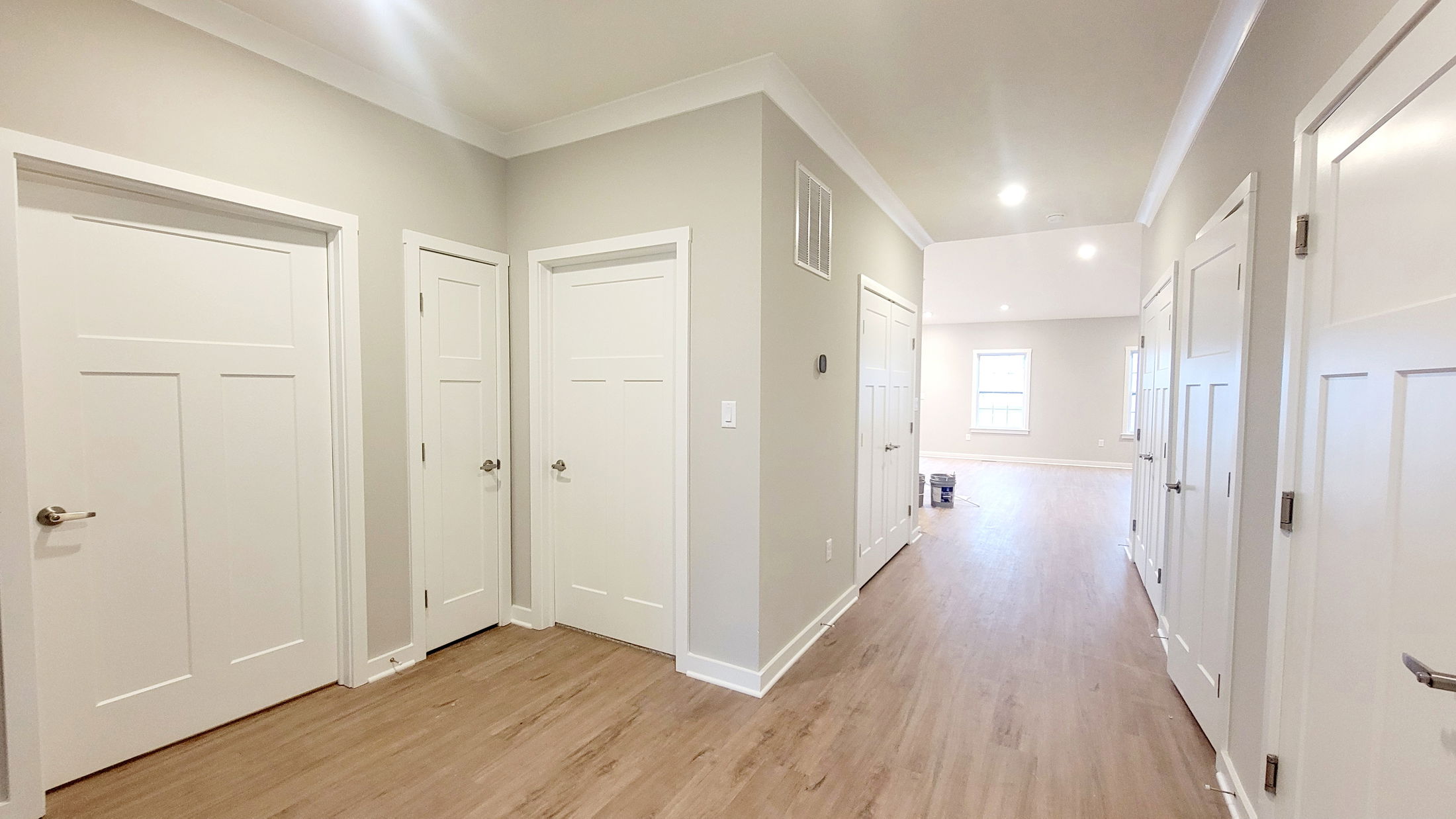 Bright and spacious hallway featuring multiple white doors, wood flooring, and recessed lighting in a modern home interior.