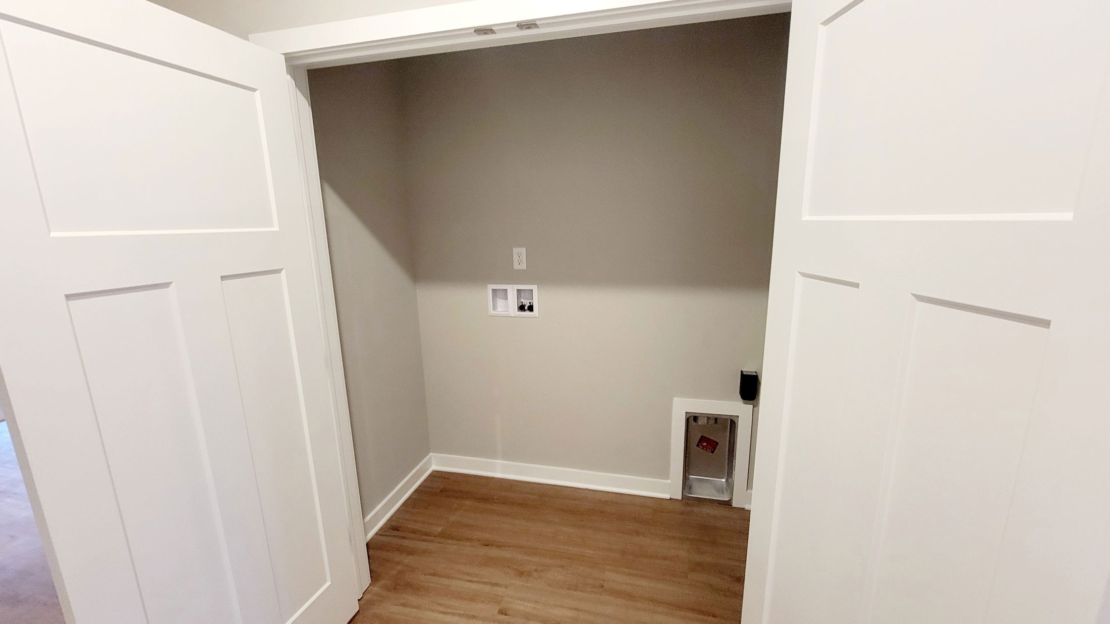 Spacious laundry room with light brown wood floor, beige walls, and white sliding doors, ready for washer and dryer installation.