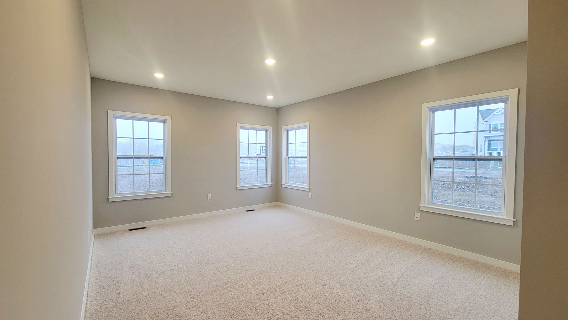 Spacious empty room with beige carpet, large windows, and recessed lighting, showcasing an inviting and bright interior.