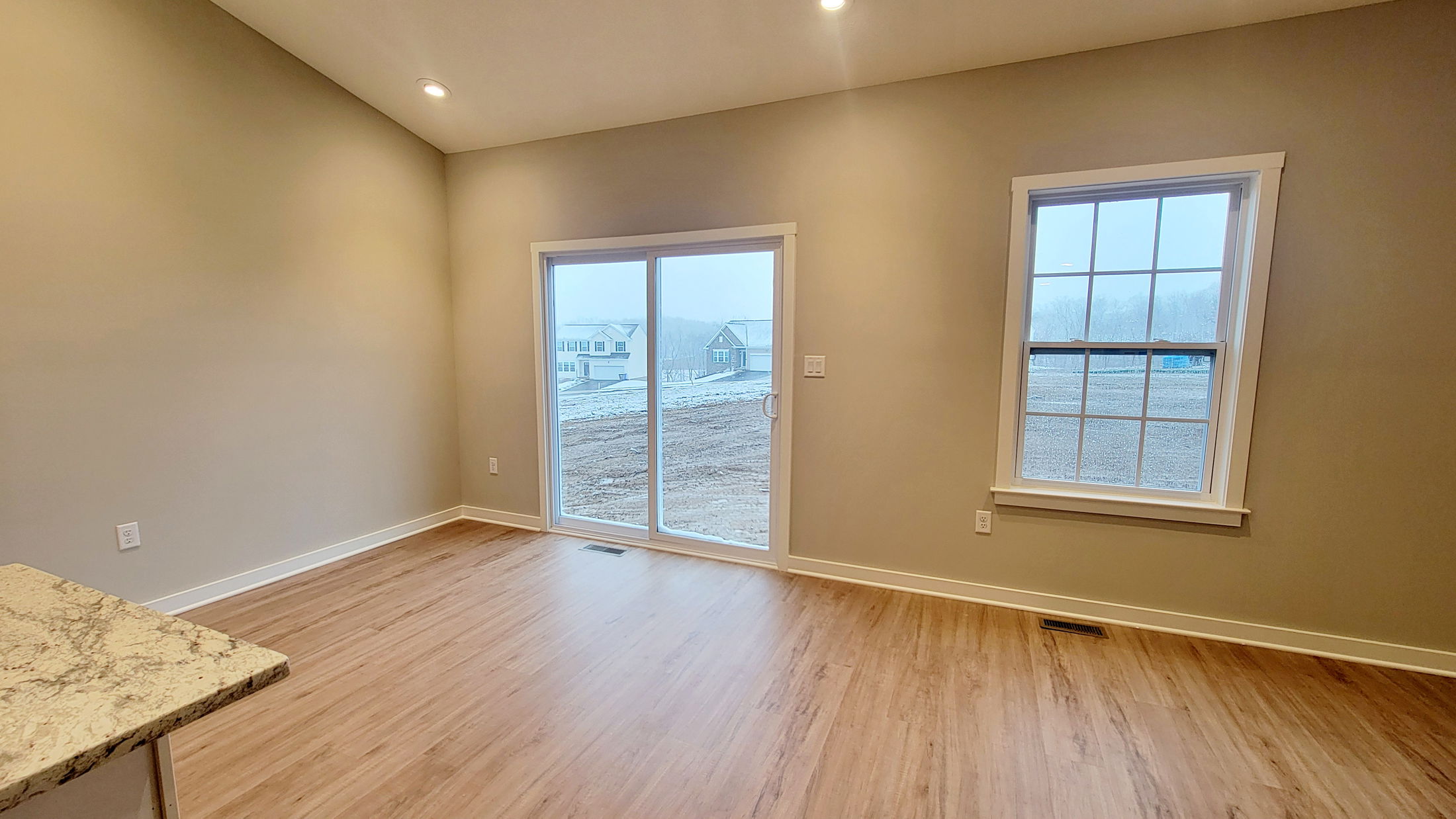 Modern interior room with light hardwood flooring, large sliding glass door, and window overlooking a snowy landscape.