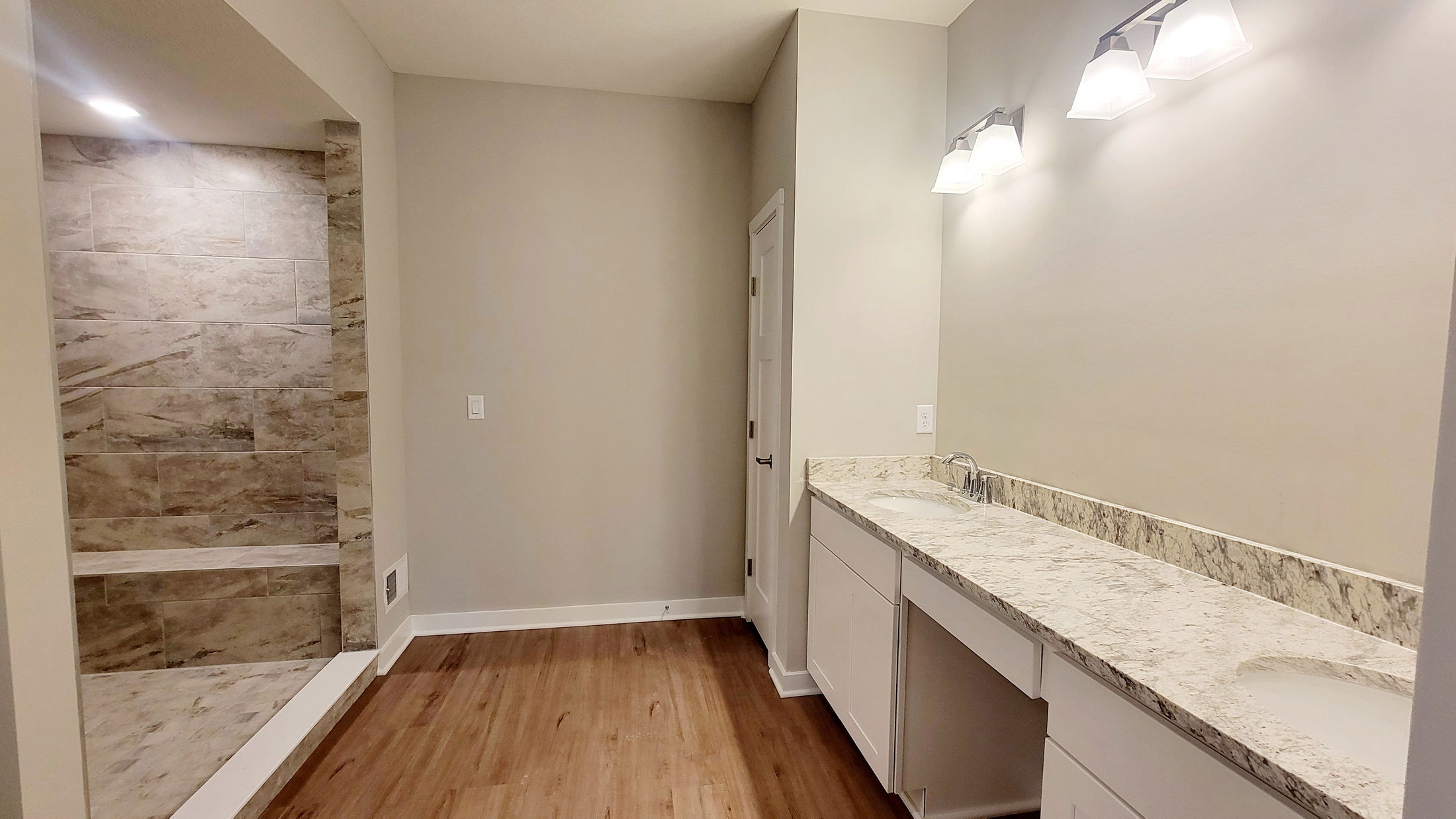 Modern bathroom featuring a marble countertop, dual sinks, tiled shower, and wooden flooring.