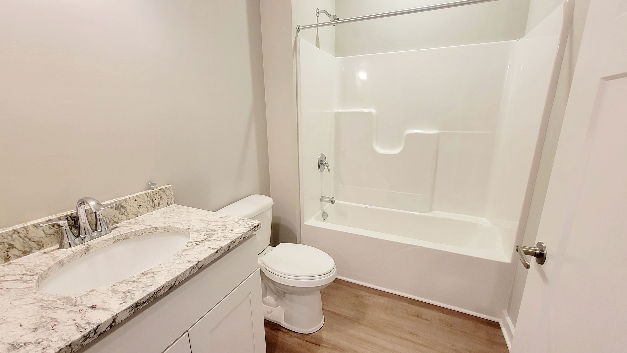 Modern bathroom with a marble countertop, white sink, toilet, and a bathtub-shower combination on hardwood flooring.